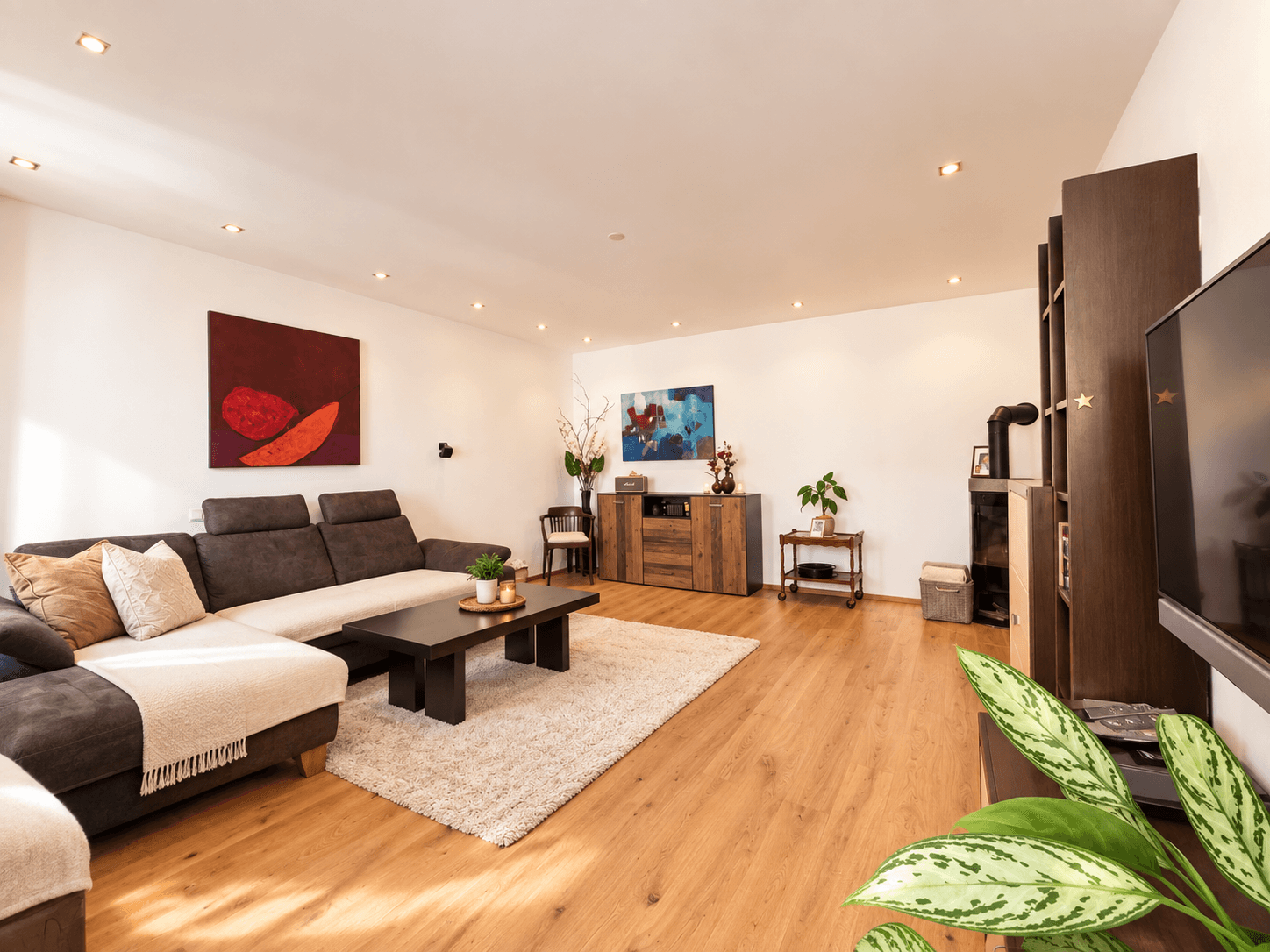 Großzügiges Wohnzimmer mit modernem Sofa, Holzboden und Kunstwerken an den Wänden.
