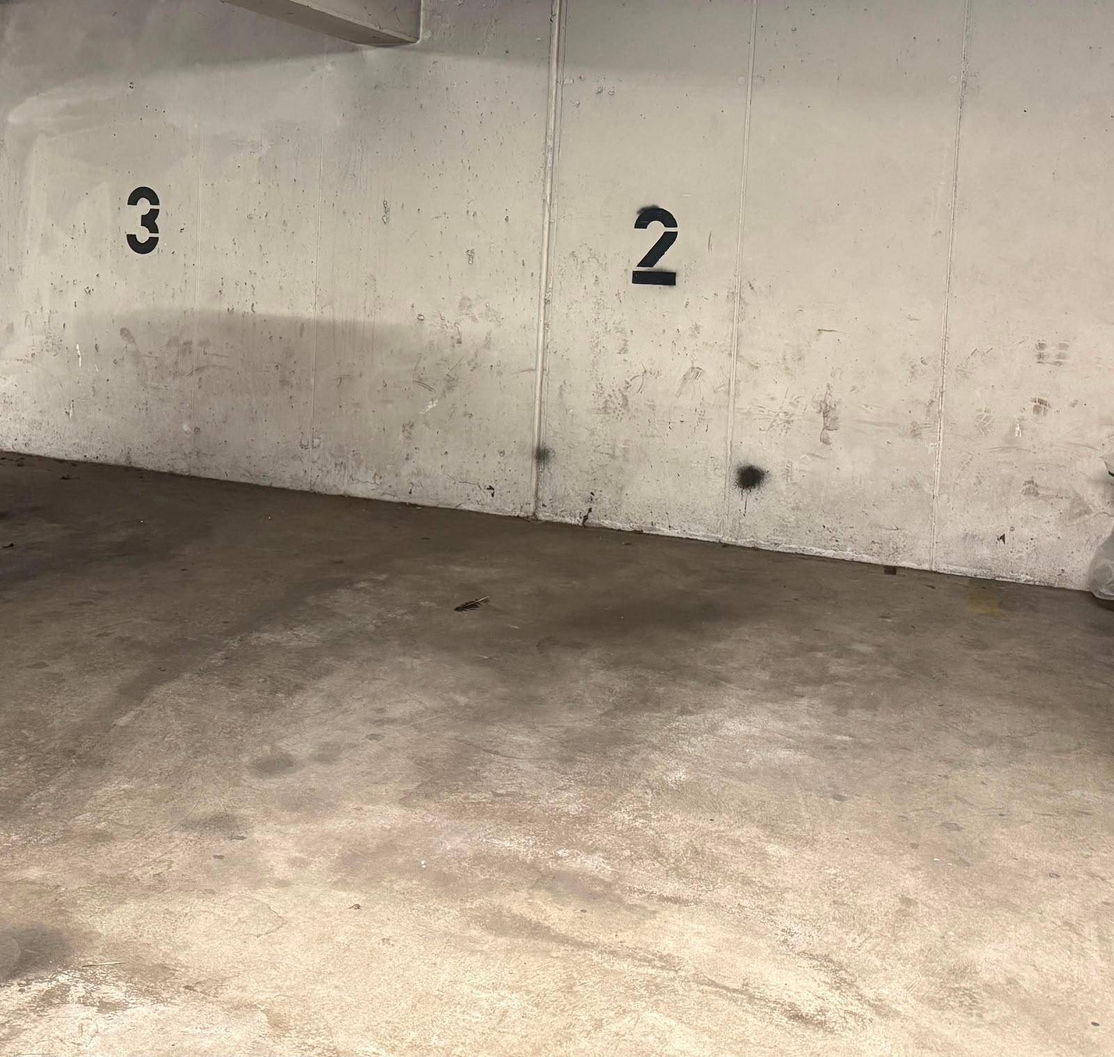 Betonwand und Boden in einer Tiefgarage mit markierten Stellplätzen.