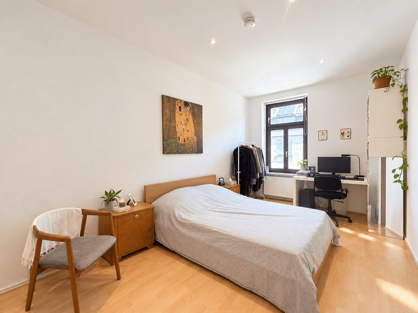 Helles Schlafzimmer mit Holzboden, Doppelbett und Arbeitsplatz am Fenster.