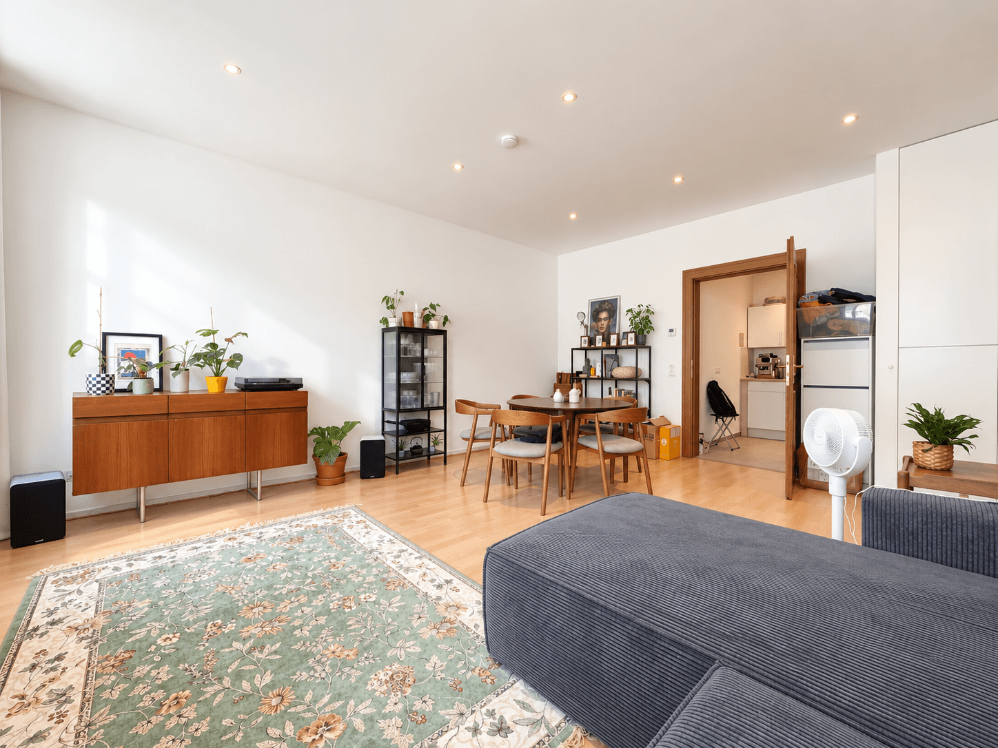 Geräumiger Wohnbereich mit Holzboden, Vintage-Sideboard und Blick in die angrenzende Küche.