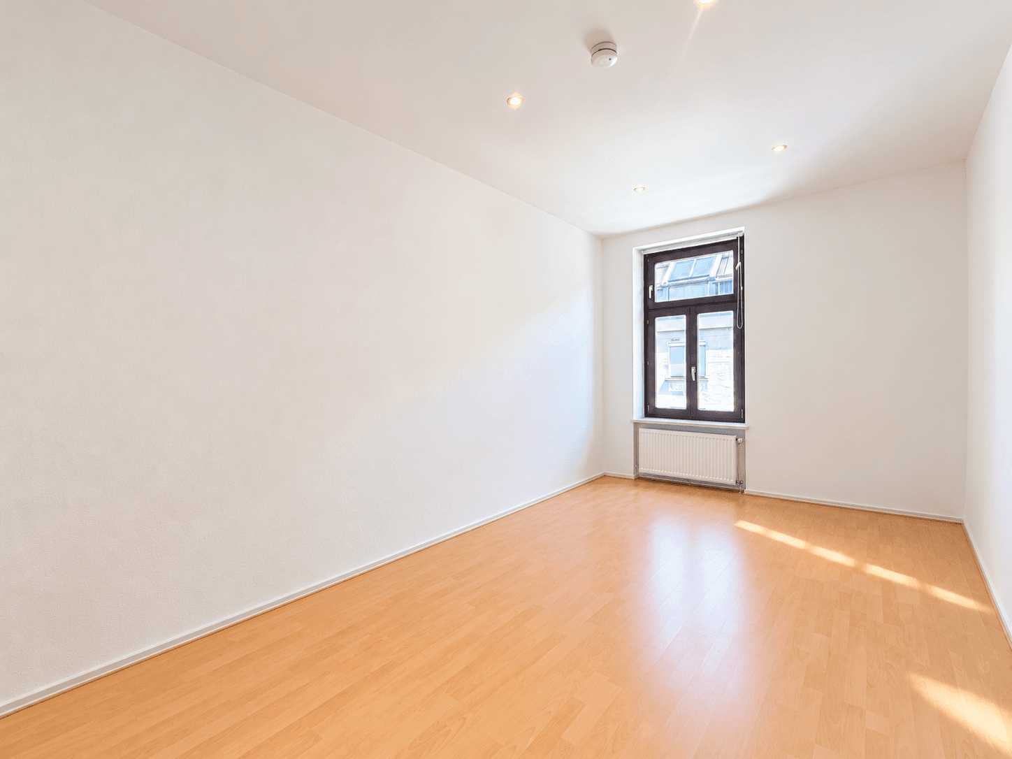 Leerer Raum mit Parkettboden und einem Fenster, das für natürliche Belichtung sorgt.