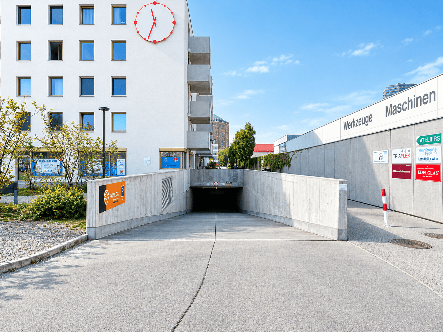 Einfahrt zu einer Tiefgarage vor einem modernen Gebäude mit großer Uhr und umliegender Infrastruktur.