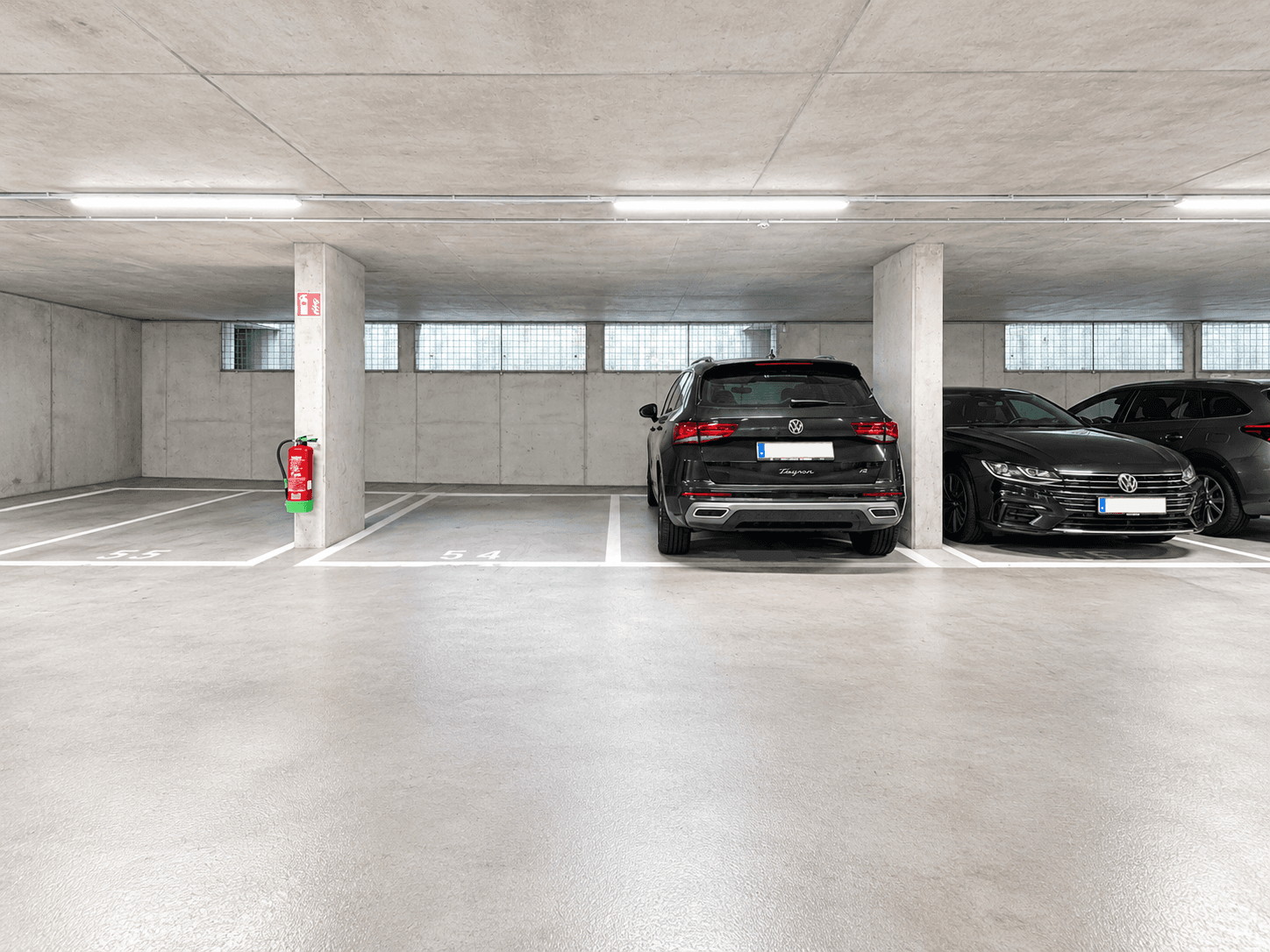 Saubere Tiefgarage mit Betonpfeilern und geparkten Fahrzeugen unter hellen Leuchten und mit Brandschutz.