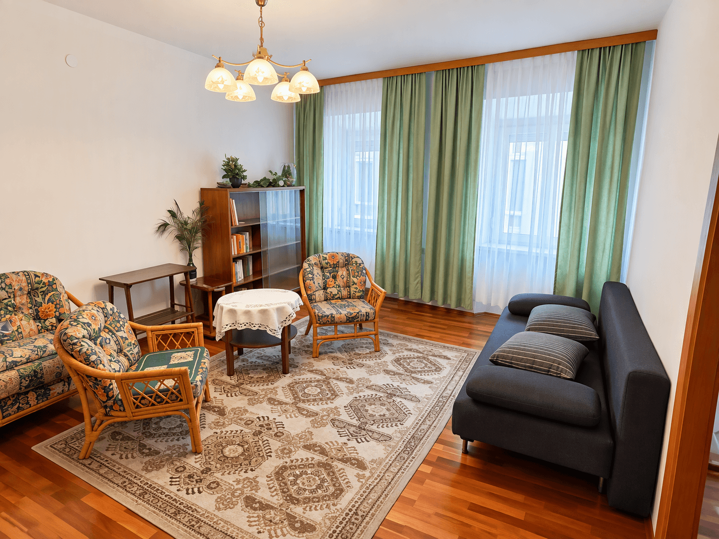 Gemütliches Wohnzimmer mit Parkettboden, floralen Sesseln und einem dunklen Sofa.