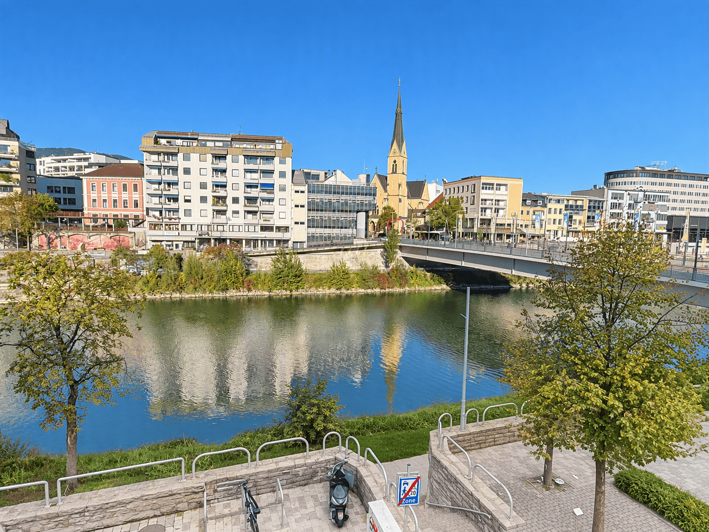 Panoramablick auf eine Stadt am Fluss mit Brücke und Kirchturm.