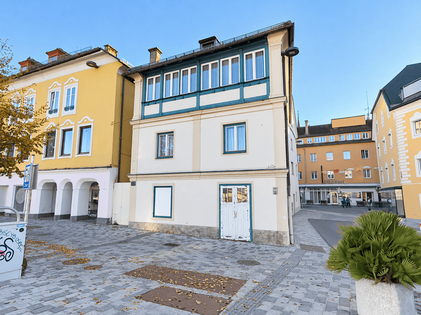 Historisches Gebäude mit beiger Fassade und blauer Holzverkleidung an einem sonnigen Tag.