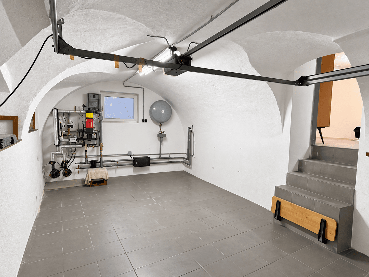 Kellerraum mit gewölbter Decke, Fliesenboden und Heizungsinstallationen.