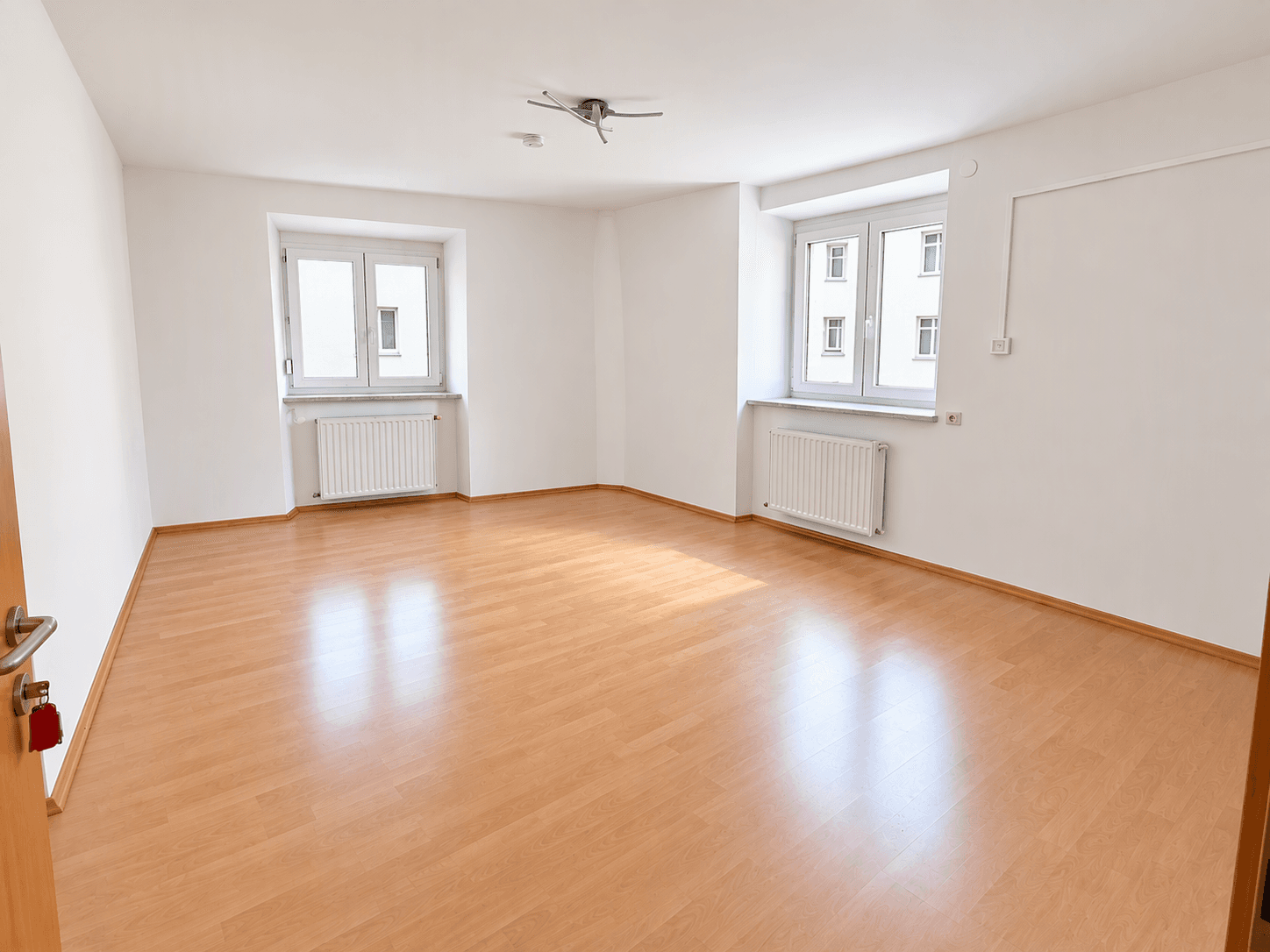 Helles, leeres Schlafzimmer mit Laminatboden und zwei Fenstern.