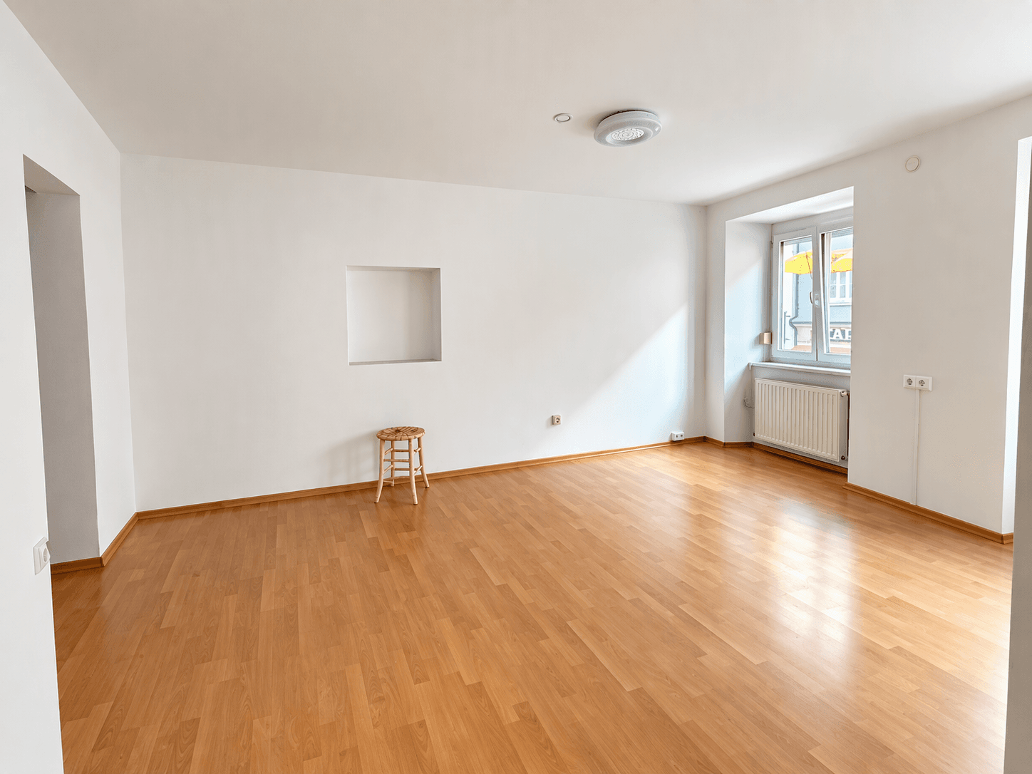 Heller, leerer Raum mit Laminatboden und einer Nische in der Wand.
