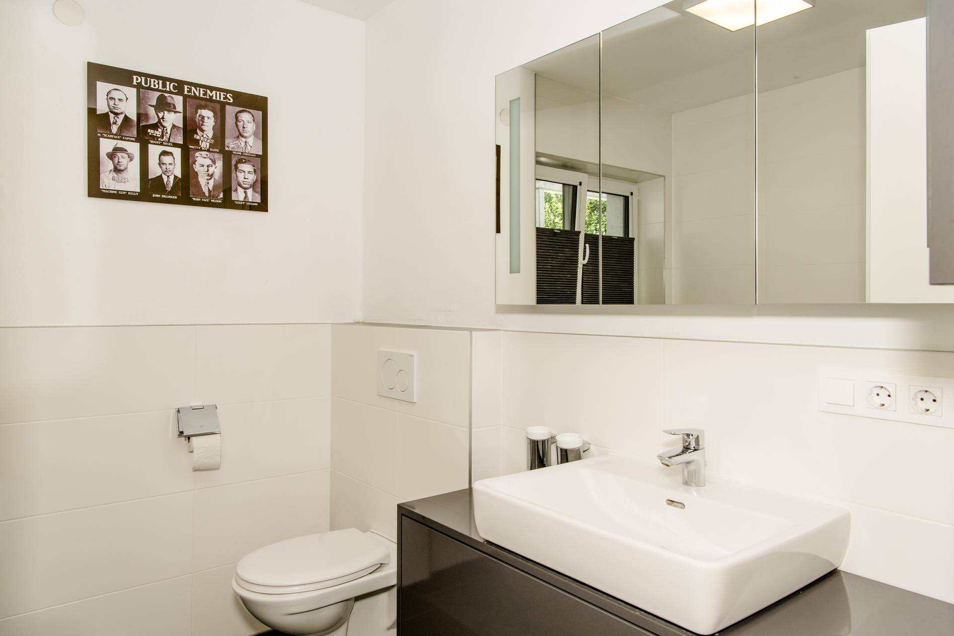 Helles Badezimmer mit modernem Waschbecken, Toilette und großem Spiegelschrank.