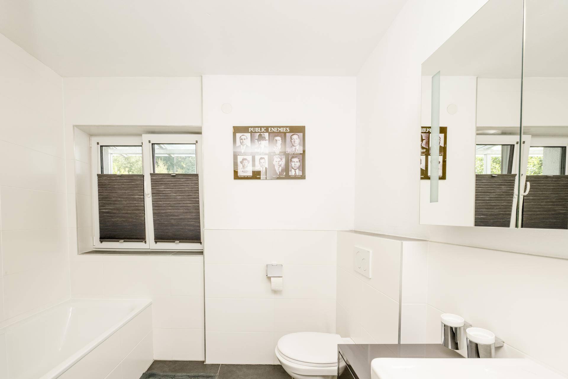 Modernes Badezimmer mit Badewanne, Toilette, Fenster und Spiegelschrank.