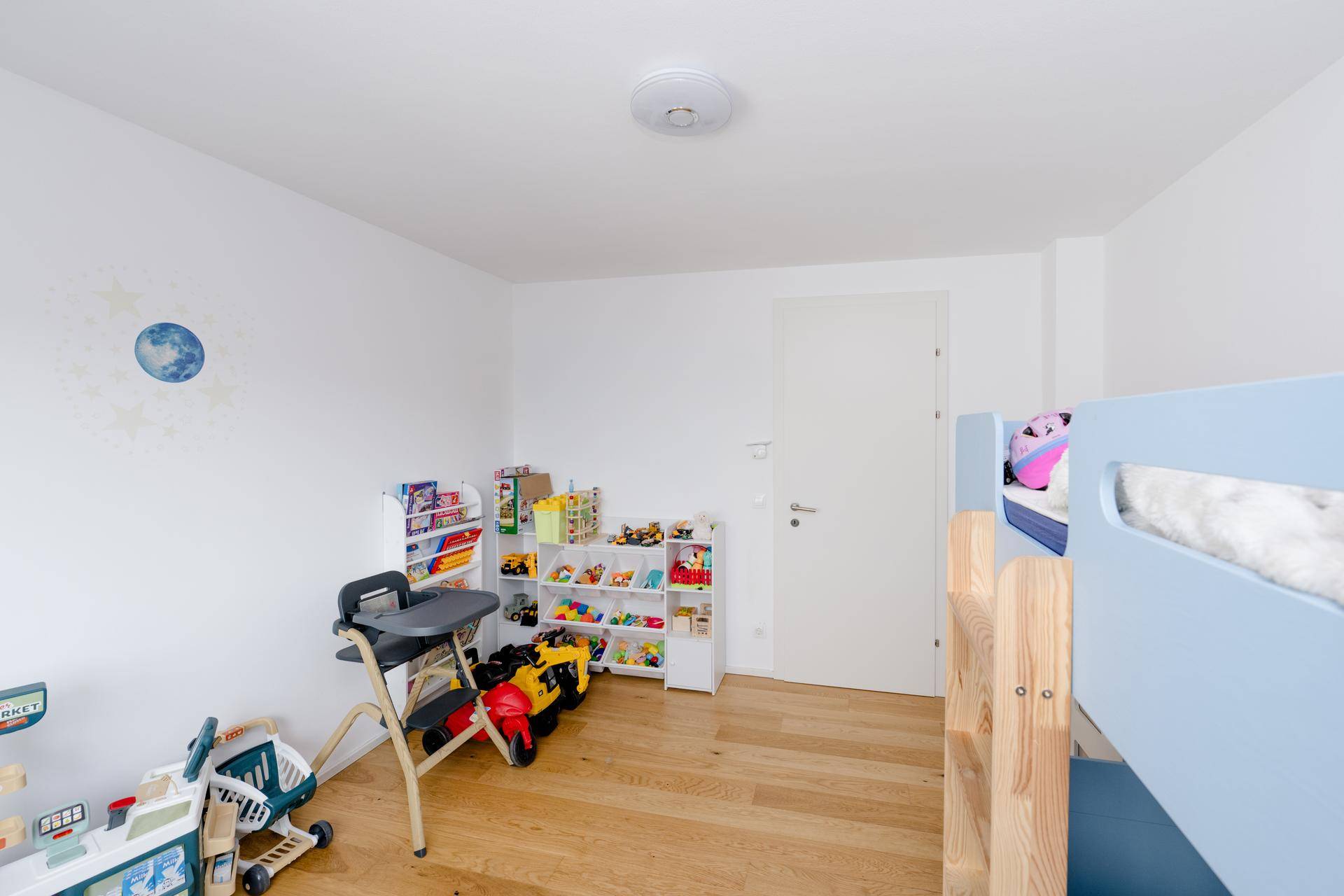 Kinderzimmer mit Etagenbett, Spielzeugregalen und hellem Holzboden.