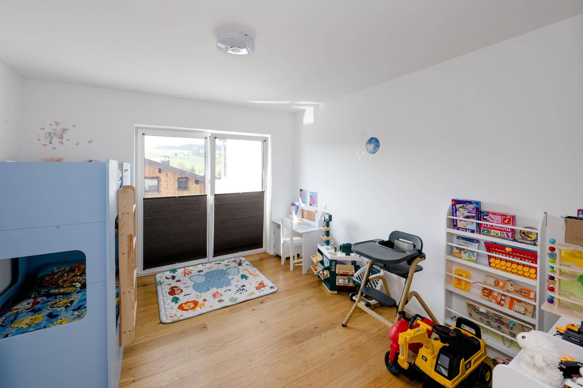 Helles Kinderzimmer mit Etagenbett, Spielzeug und Fenster mit Blick ins Grüne.