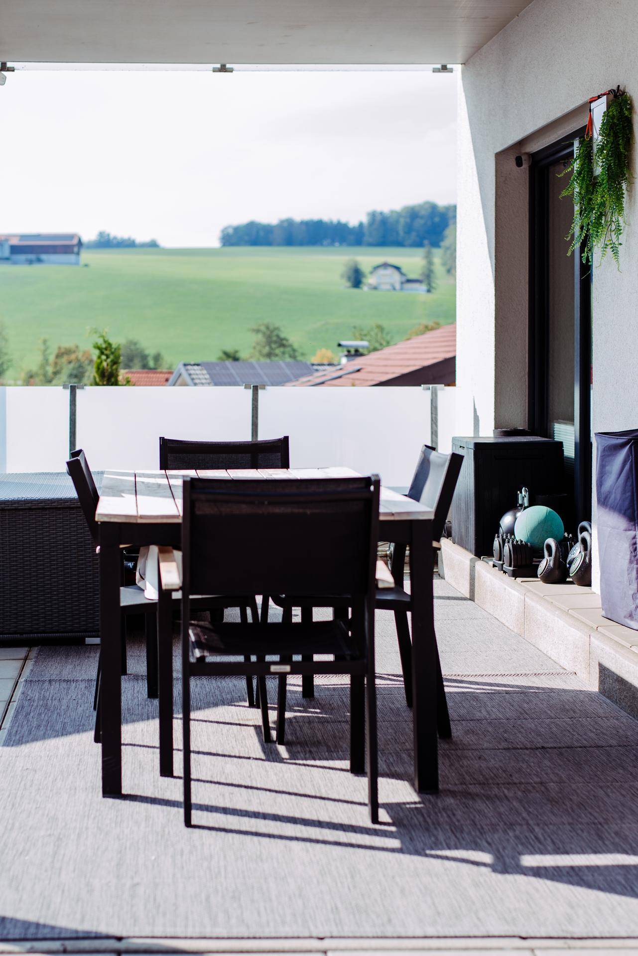 Überdachter Terrassenbereich mit Esstisch und Stühlen, bietet weiten Blick ins Grüne.