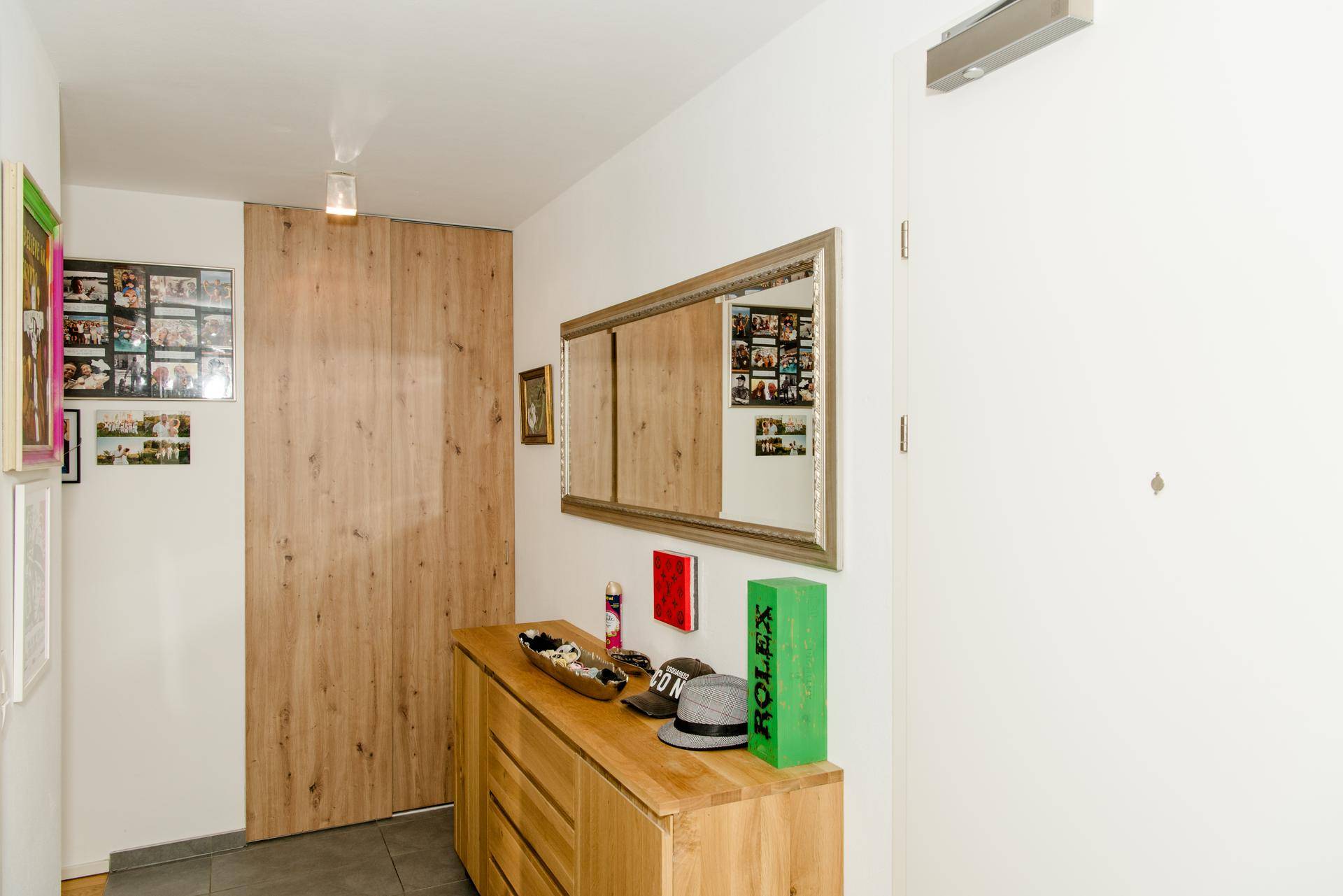 Heller Eingangsbereich mit Holzkommode, großem Spiegel und Holztür.