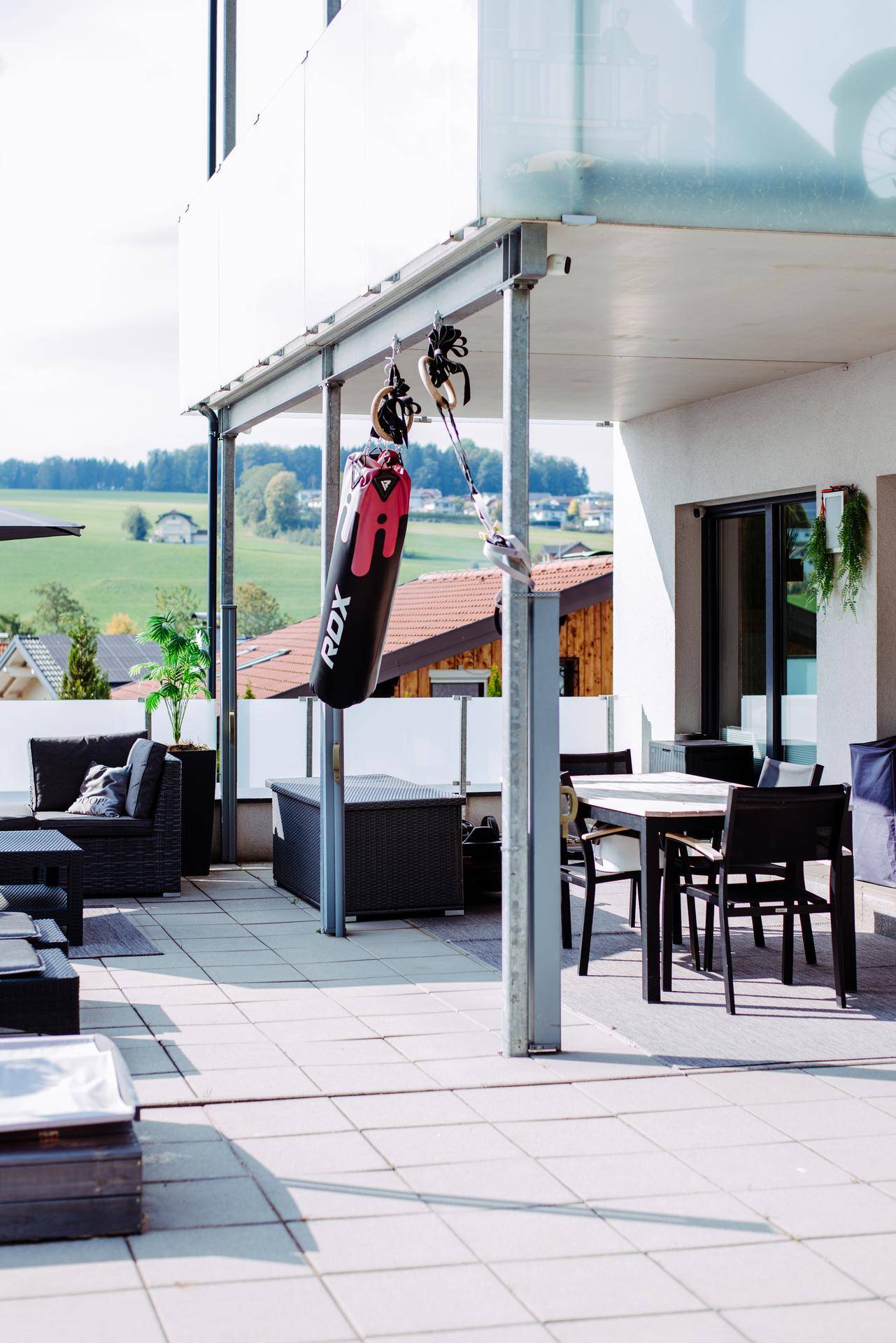 Große geflieste Terrasse mit Sitzgelegenheiten, Boxsack und weitem Blick ins Grüne.
