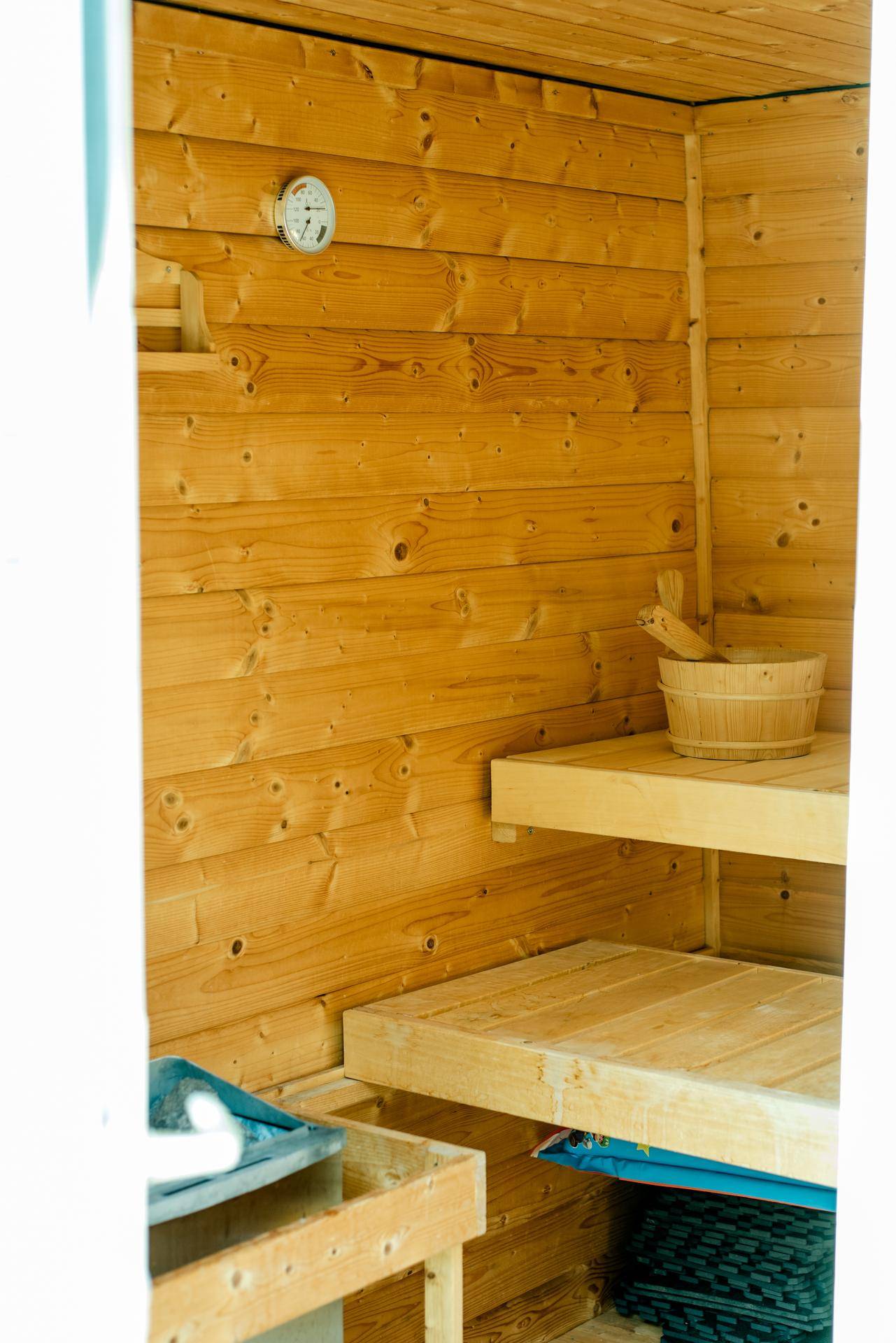 Innenansicht einer Holzsauna mit Bänken, Thermometer und traditionellem Eimer.