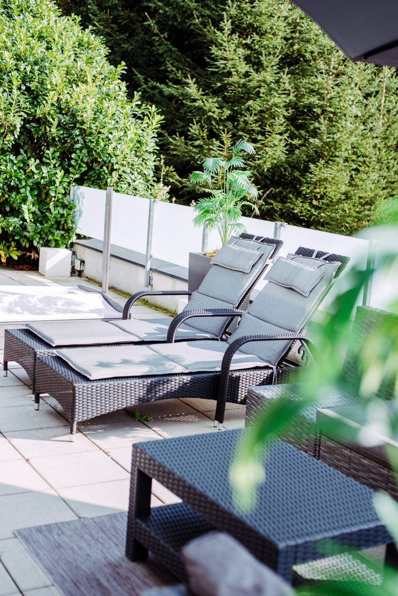Entspannungsbereich auf der Terrasse mit Liegestühlen, Pflanzen und Sonnenschirm.