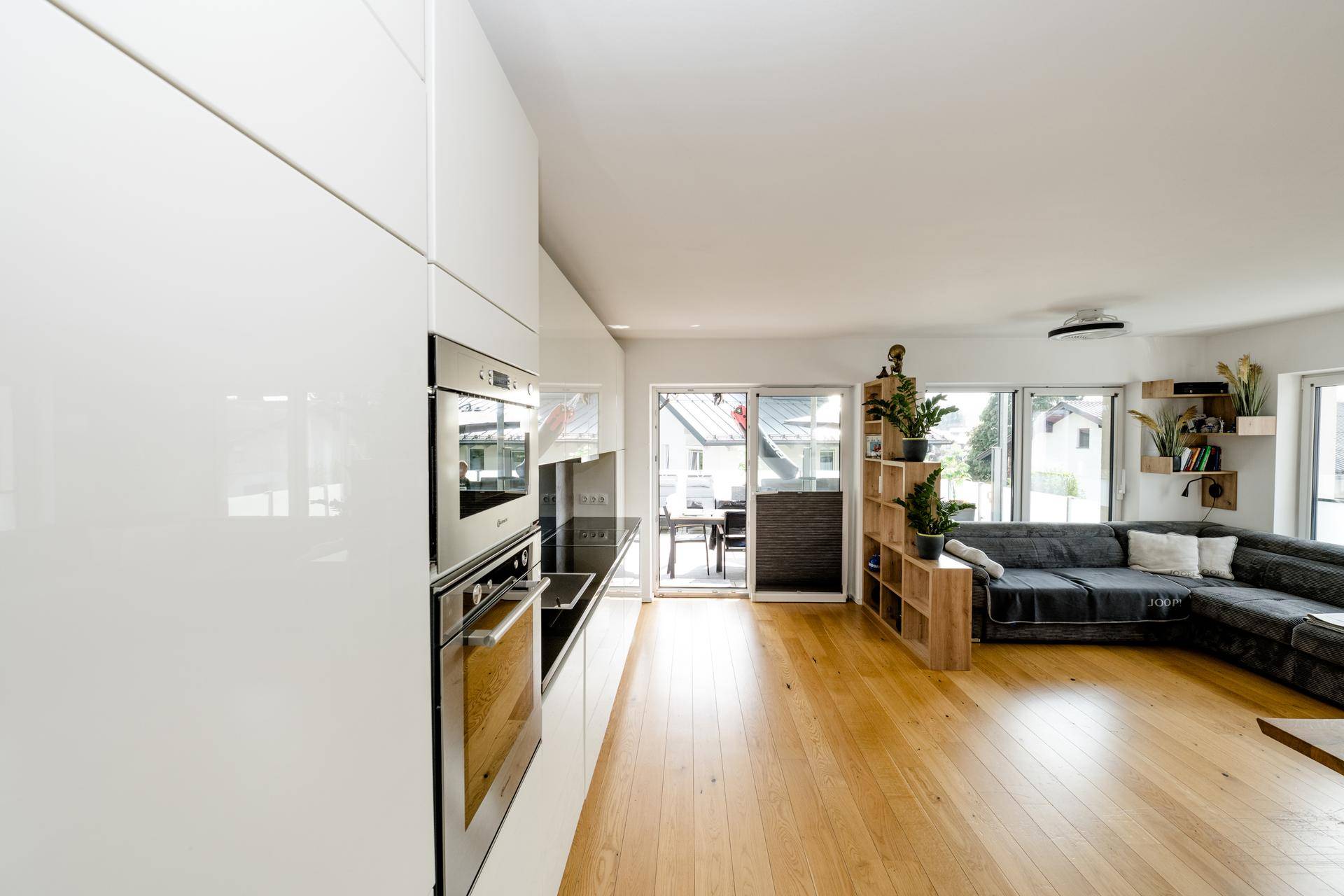 Moderner Wohnbereich mit integrierter Küche, Sofa und großen Schiebetüren zur Terrasse.