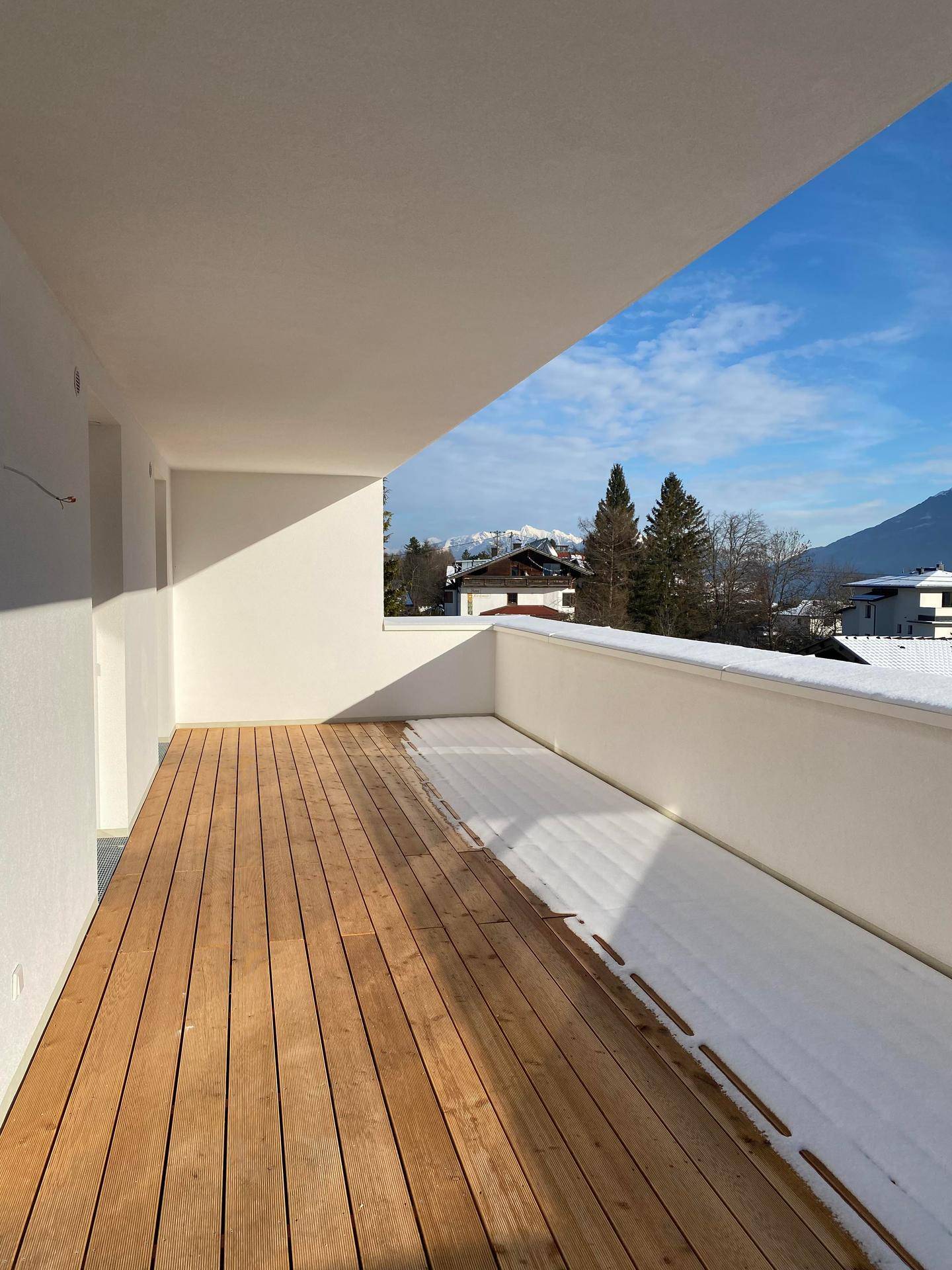 Breiter Balkon mit Holzboden und Bergblick, teilweise mit Schnee bedeckt.