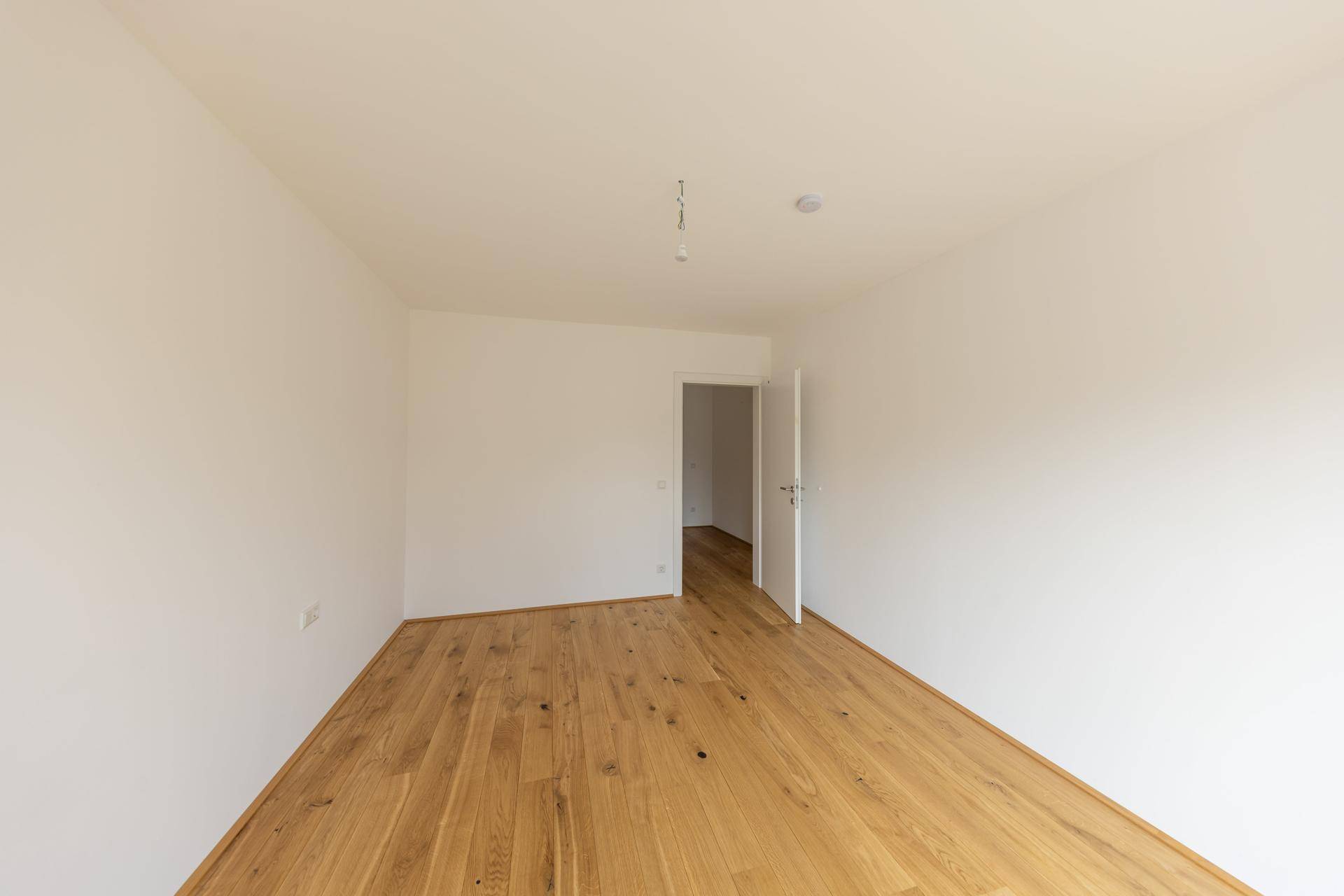 Unmöbliertes Zimmer mit Holzboden und weiß gestrichenen Wänden, bereit zur individuellen Gestaltung.