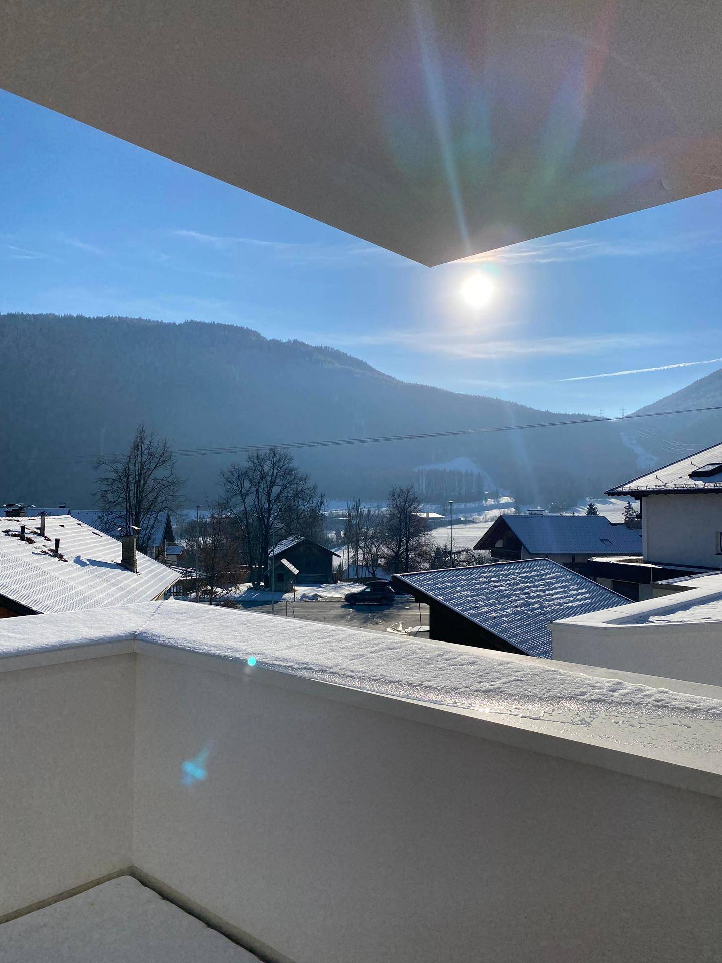 Sonnige Balkonaussicht auf schneebedeckte Berge und die umliegende Landschaft.