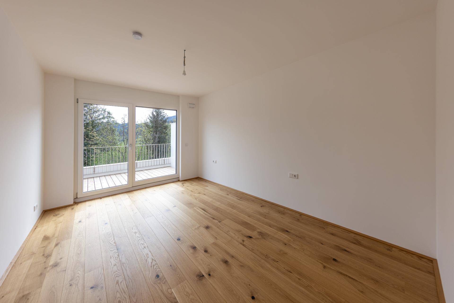 Leeres Schlafzimmer mit Holzboden und Zugang zu einem Balkon, hell und geräumig.