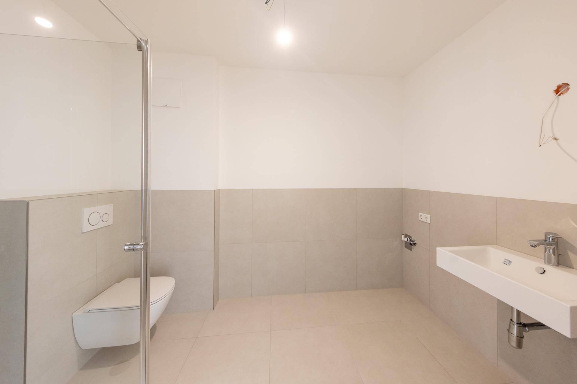 Helles Badezimmer mit Wand-WC, Waschbecken und modernen Fliesen in neuwertigem Zustand.