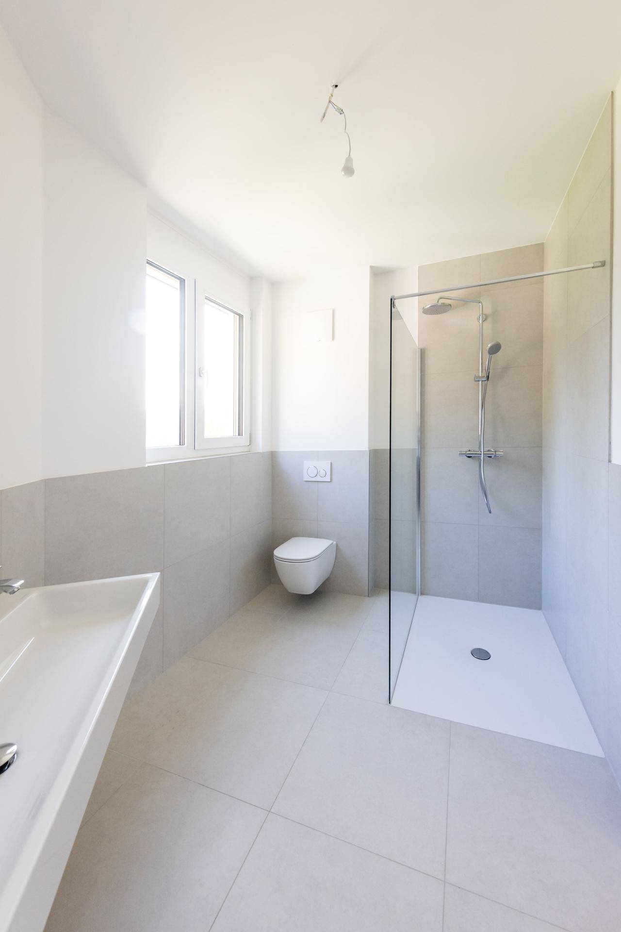 Modernes Badezimmer mit bodengleicher Dusche, wandhängendem WC und großem Fenster.
