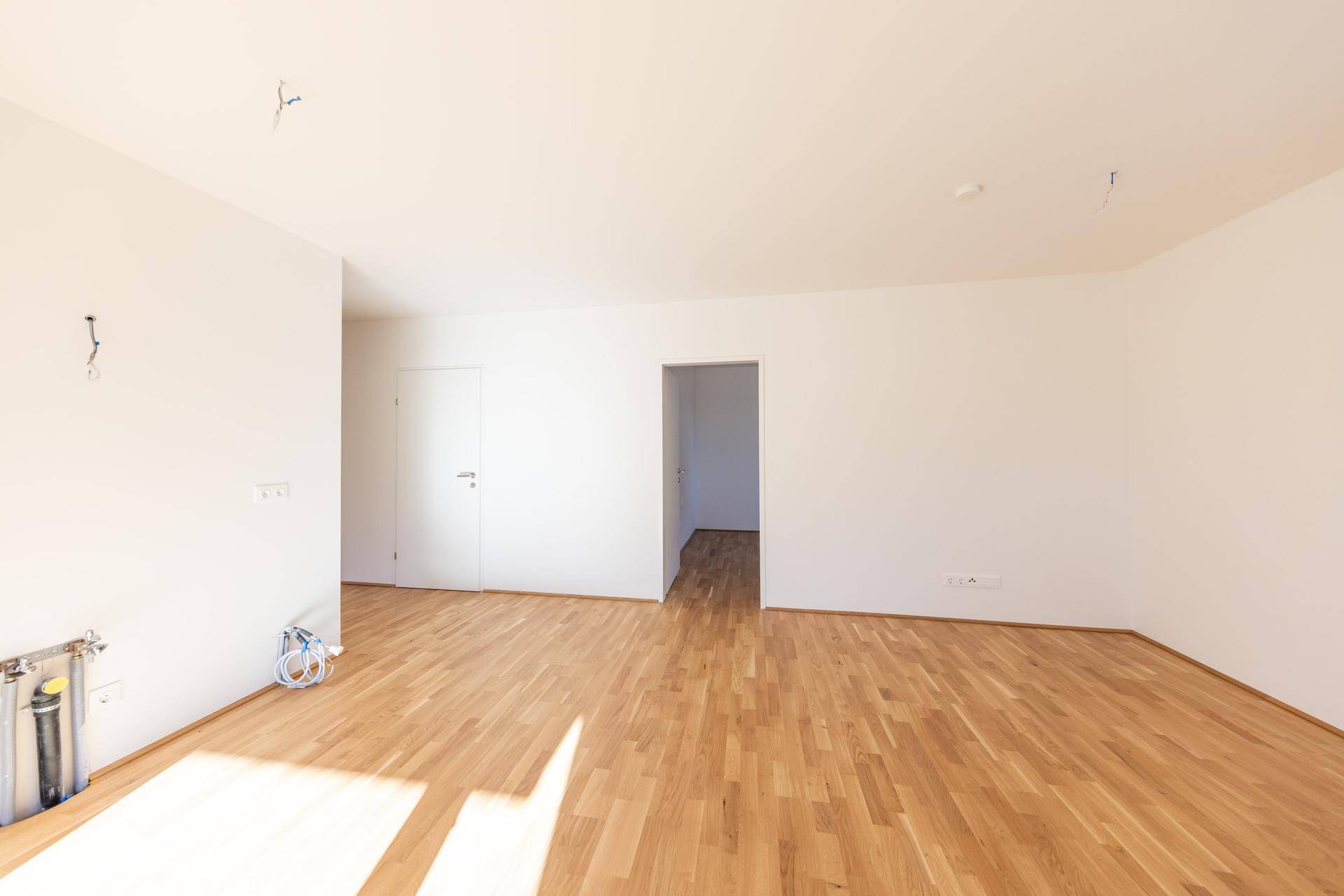 Helles, unmöbliertes Zimmer mit Parkettboden und vorbereiteten Anschlüssen für die Einrichtung.