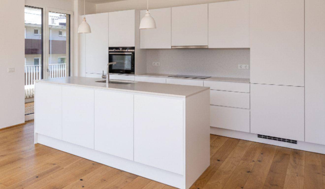 Moderne weiße Einbauküche mit Kücheninsel, integrierten Geräten und Holzboden.