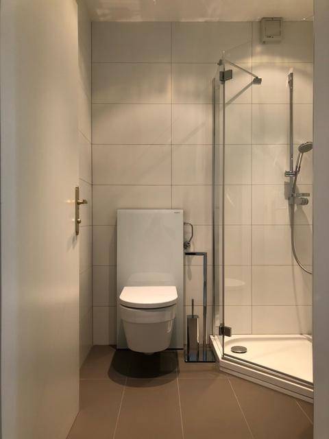 Modernes Badezimmer mit Duschkabine, wandhängendem WC und hellen Fliesen.