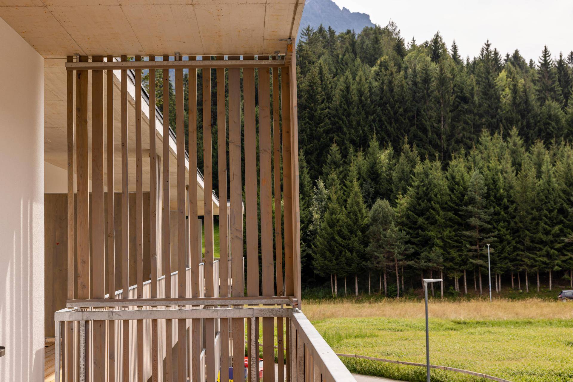 Balkon mit Holzlamellen-Brüstung und weitem Blick auf dichte Wälder und die umliegenden Berge.