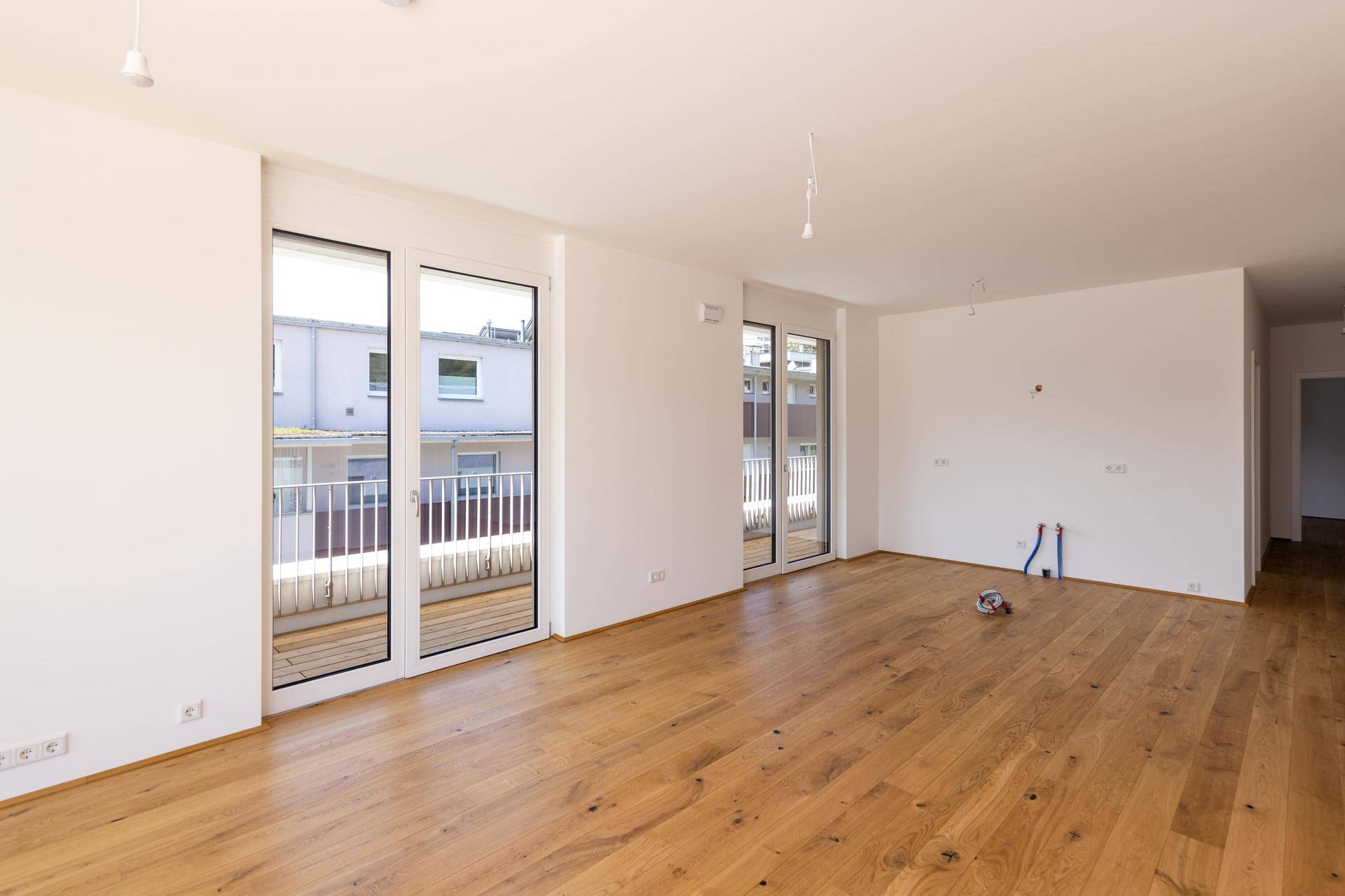 Heller, leerer Wohnraum mit Holzboden und Zugang zu einem Balkon.
