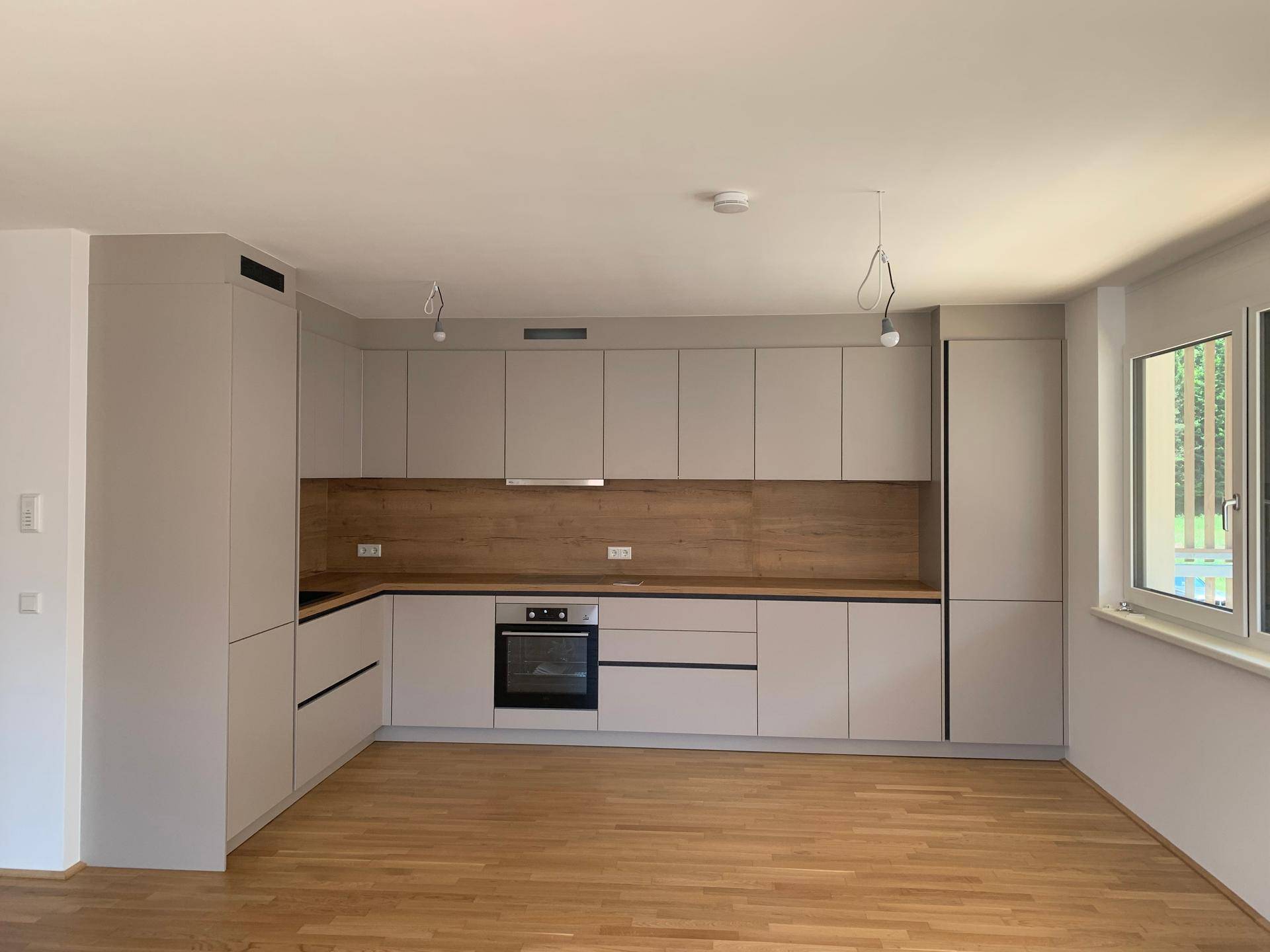 Moderne Einbauküche in Hellgrau mit Holzdetails und integriertem Backofen, bereit zur Nutzung.