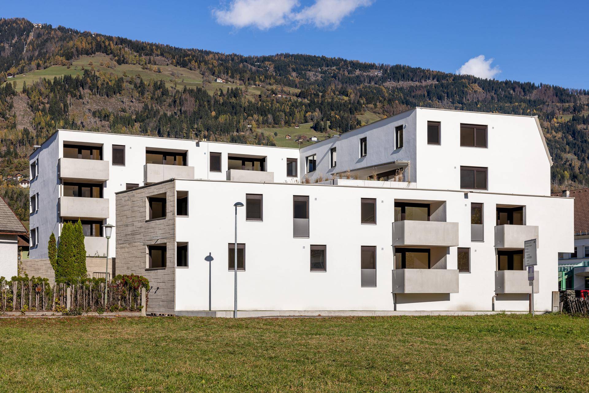 Moderne Wohnanlage mit weißer Fassade, Balkonen und Blick auf die grüne Hügellandschaft.