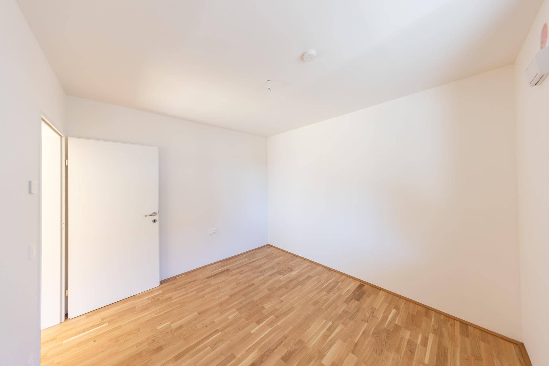 Leeres Schlafzimmer mit hellem Parkettboden und weiß gestrichenen Wänden, bereit zur individuellen Gestaltung.