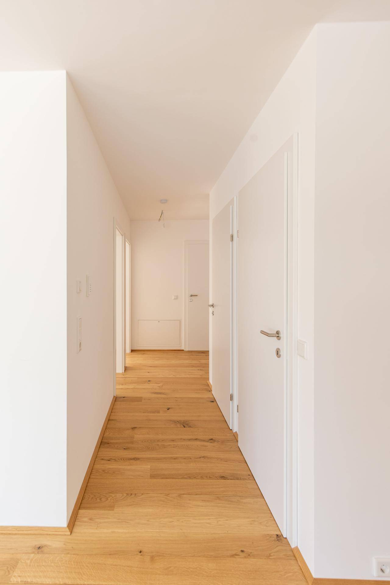 Heller Flur mit Holzboden und weißen Türen, der zu weiteren Räumen führt.