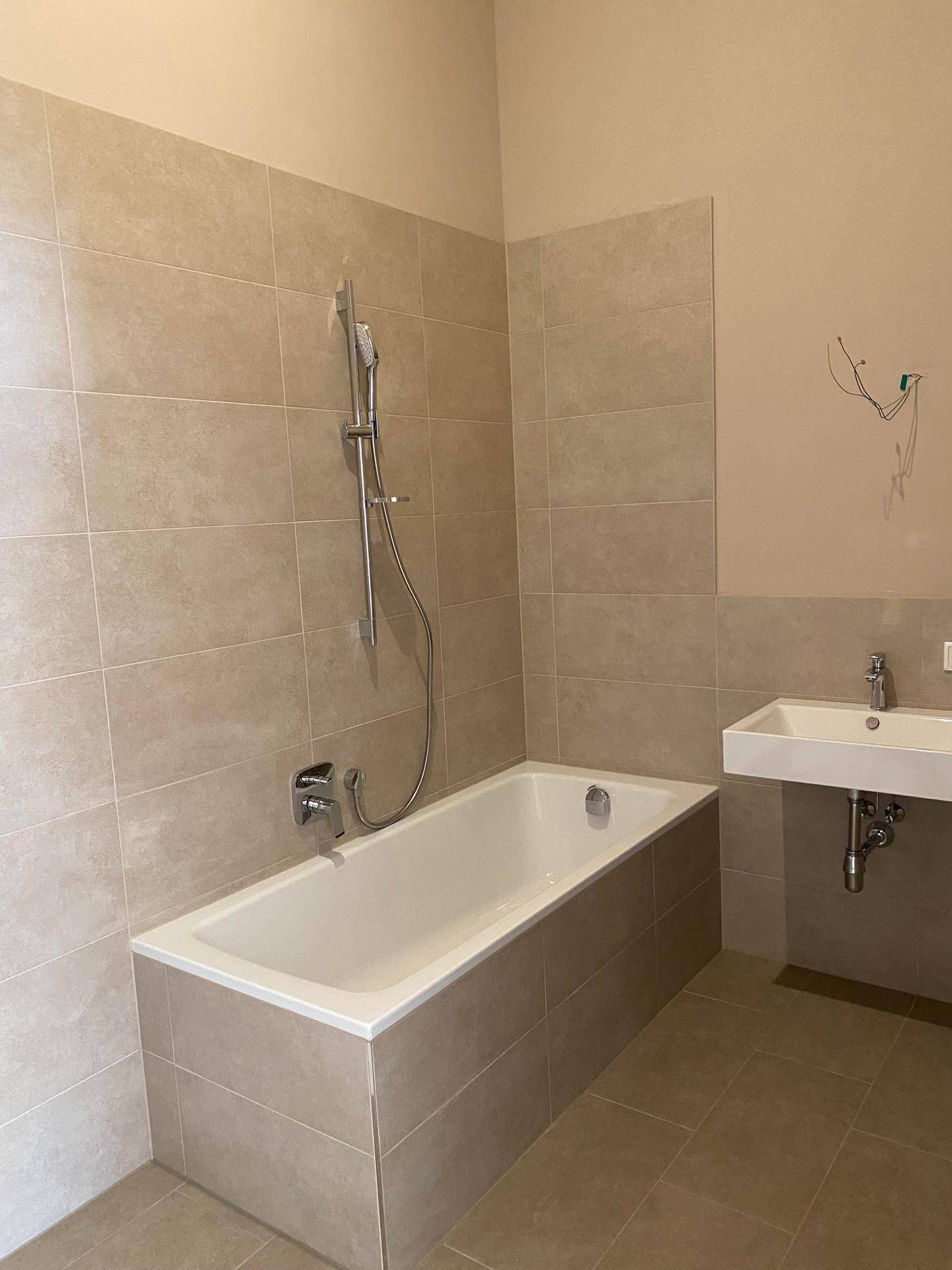 Modernes Badezimmer mit Badewanne, Waschbecken und beigefarbenen Fliesen.