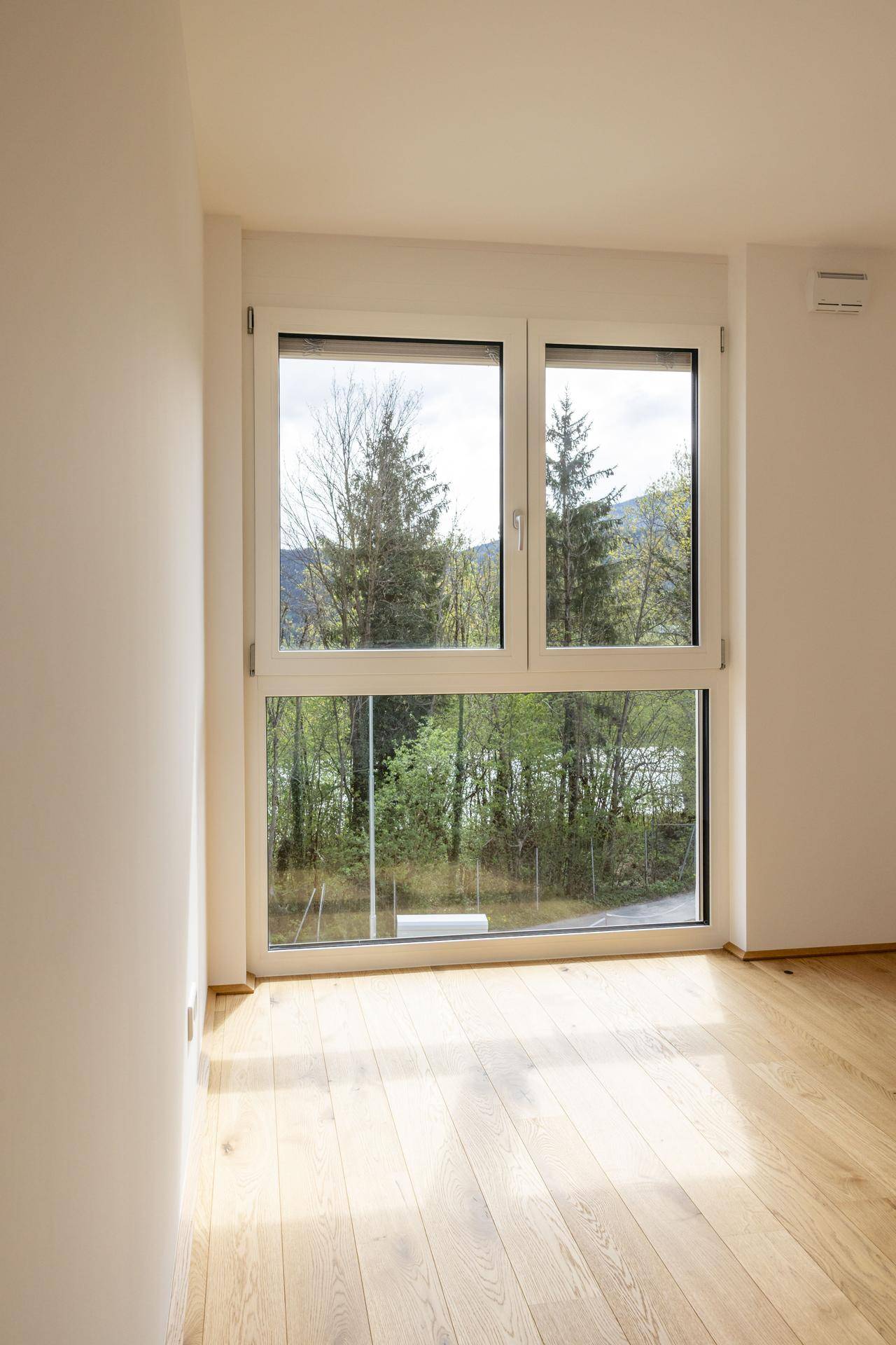 Lichtdurchfluteter Raum mit Holzboden und großem Fenster, das einen weiten Blick ins Grüne bietet.
