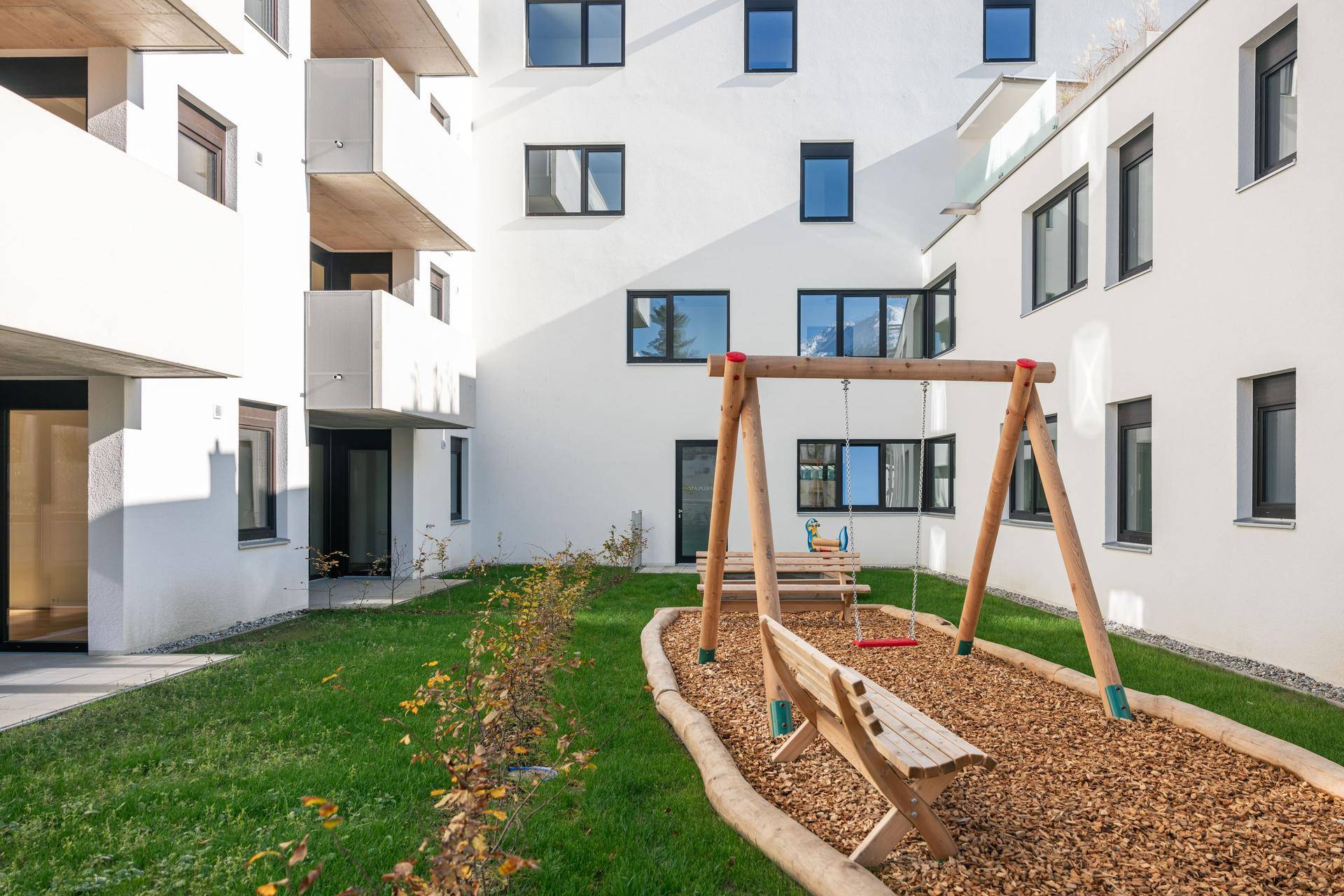 Moderner Innenhof mit Kinderspielplatz, Schaukel und Sitzbänken, umgeben von Wohngebäuden.