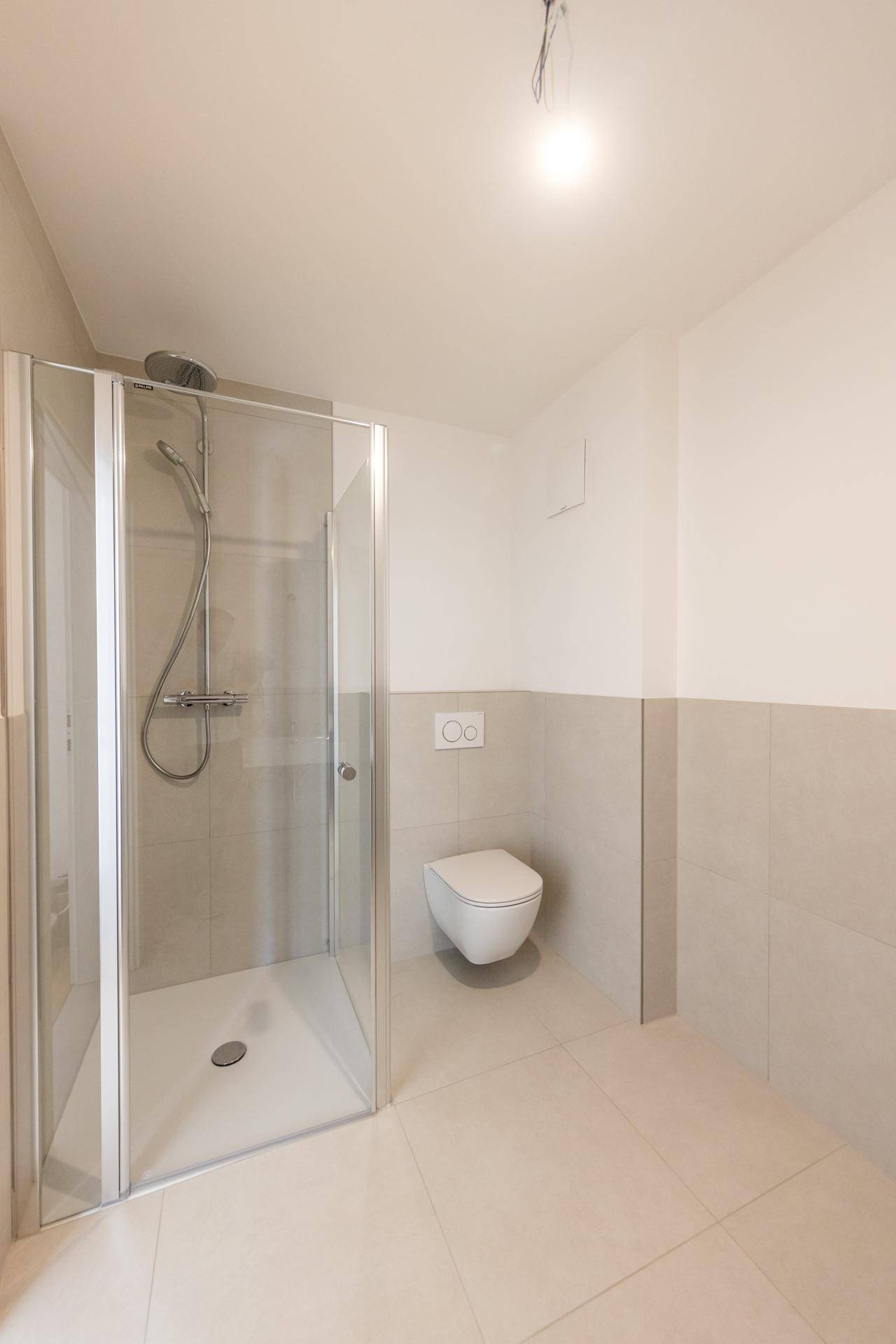 Modernes Badezimmer mit Duschkabine, Wand-WC und hellen Fliesen in neuwertigem Zustand.