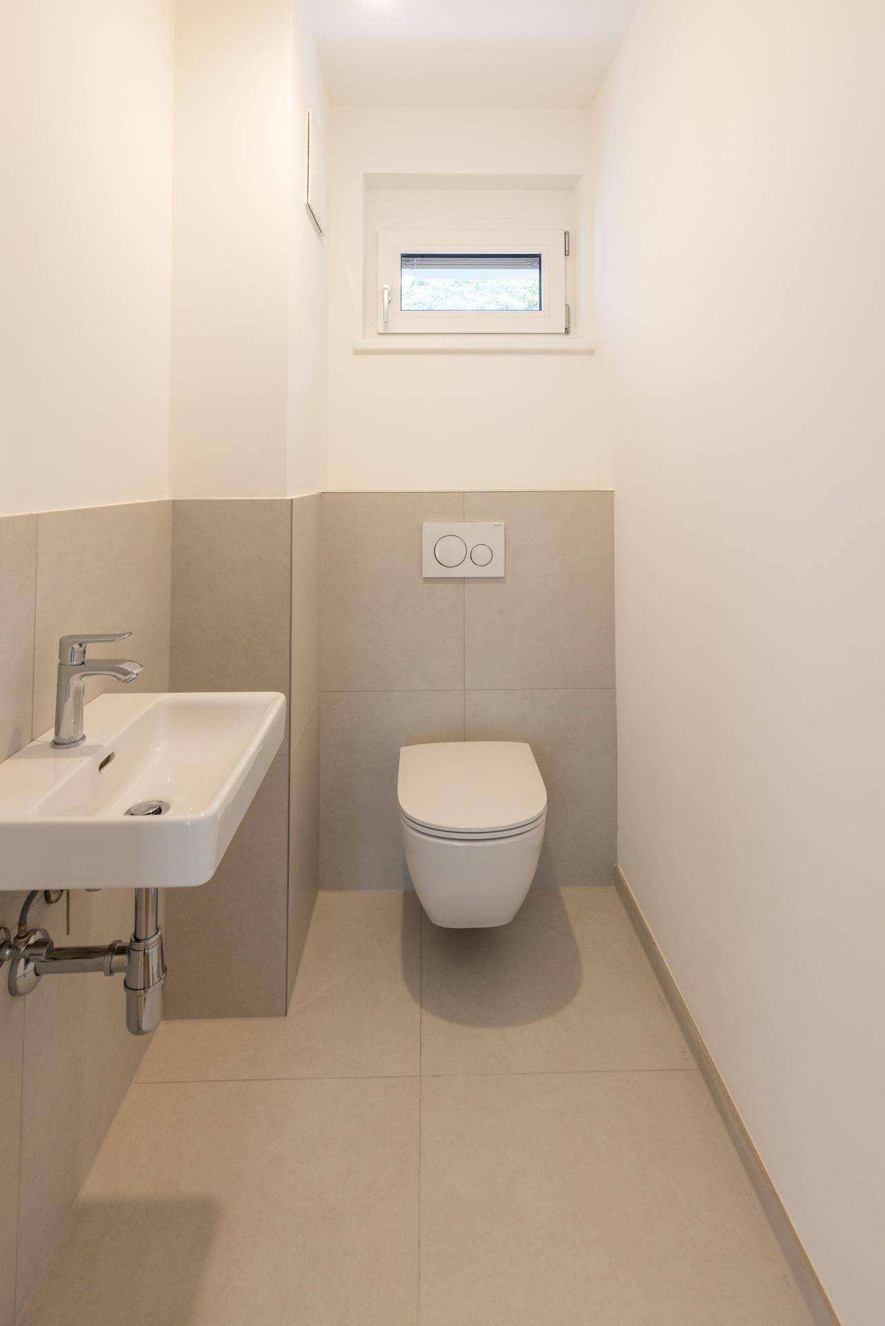 Modernes Gäste-WC mit wandhängender Toilette, kleinem Waschbecken und Fenster.