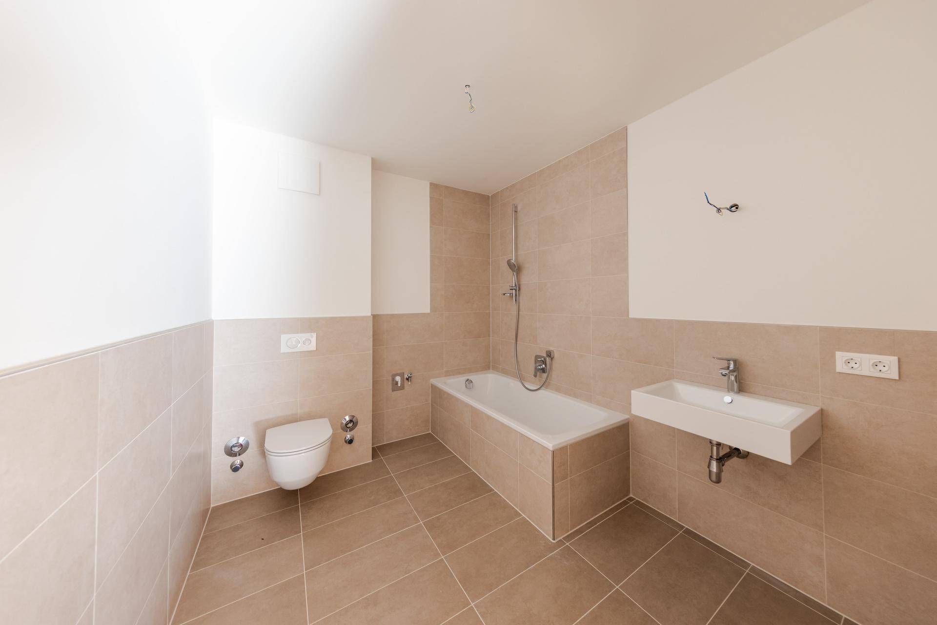 Modernes Badezimmer mit beigefarbenen Fliesen, Badewanne, wandhängendem WC und Waschbecken.