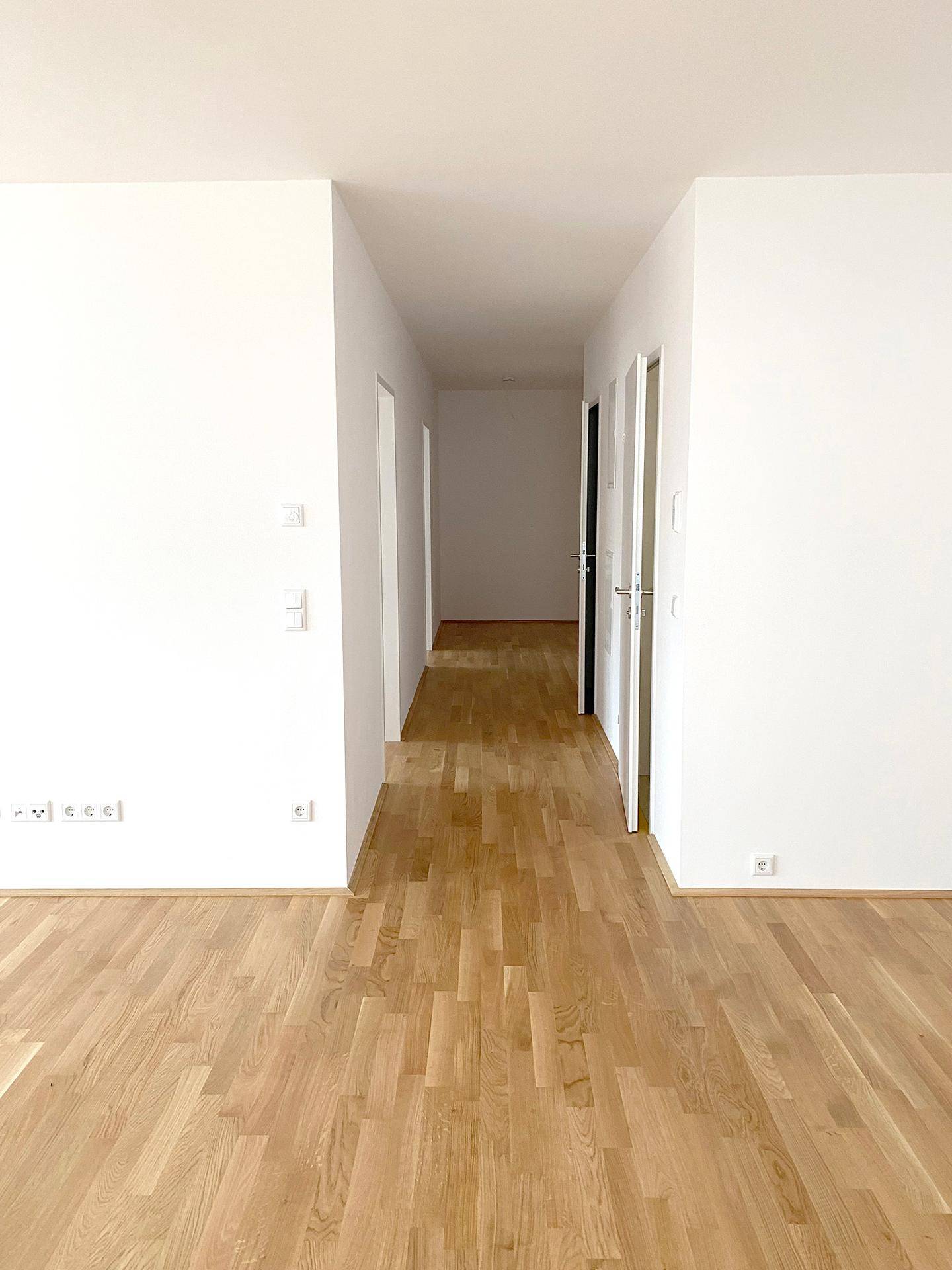 Heller Flur mit Eichenparkett und weißen Wänden, der zu weiteren Zimmern der Wohnung führt.