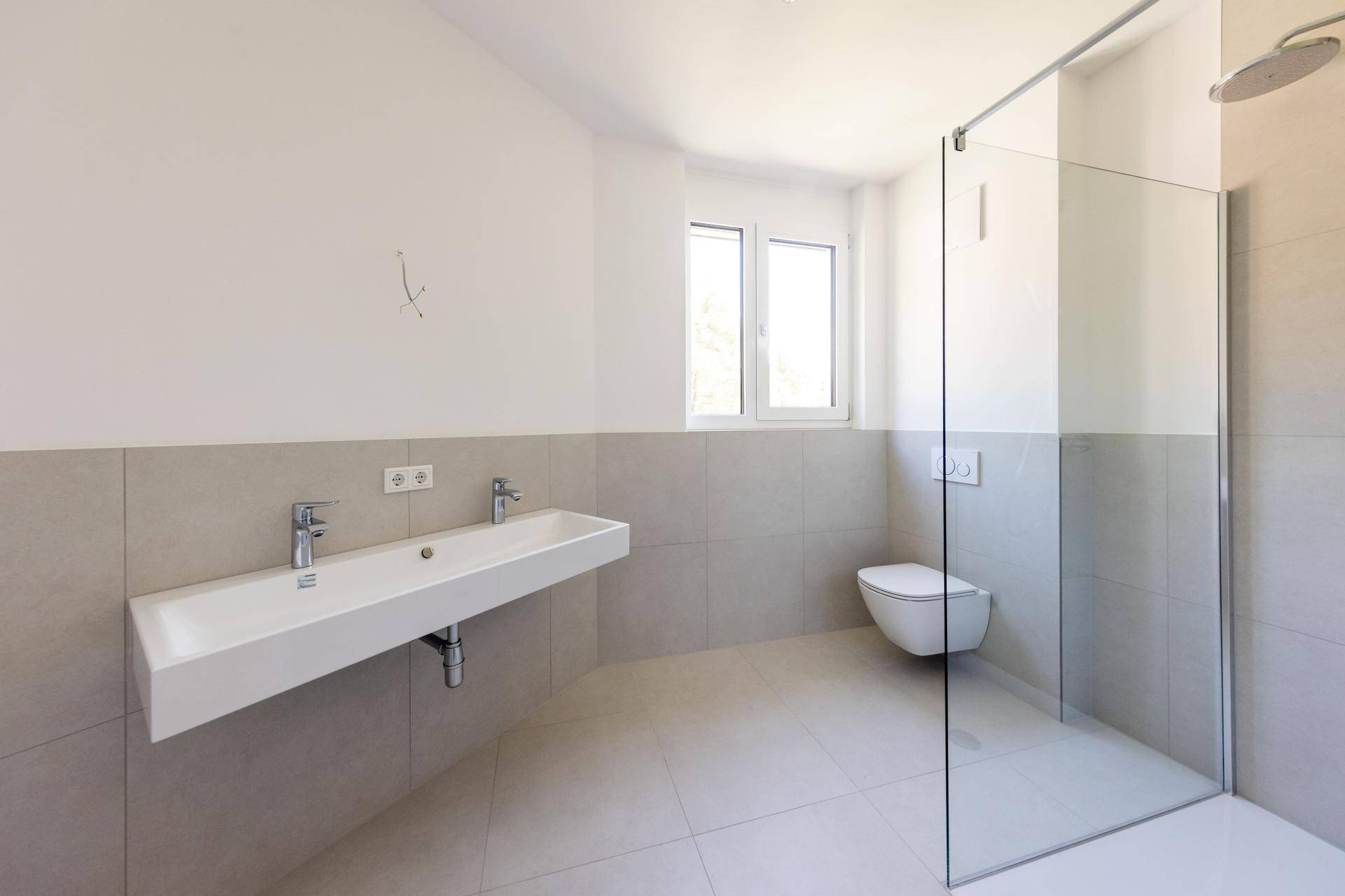 Modernes Badezimmer mit Doppelwaschbecken, bodengleicher Dusche und hellen Fliesen.