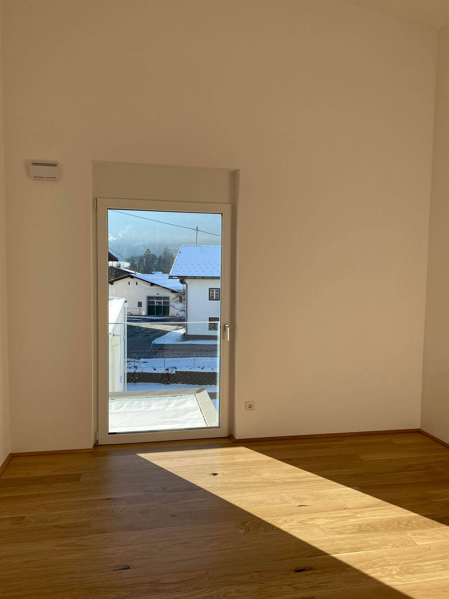 Helles Zimmer mit Holzboden und französischem Balkon, bietet Blick auf die Umgebung.