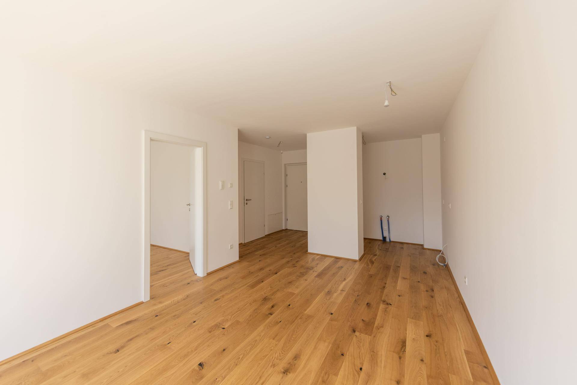 Leerer Raum mit Holzboden und weißen Wänden, bereit für die individuelle Gestaltung.