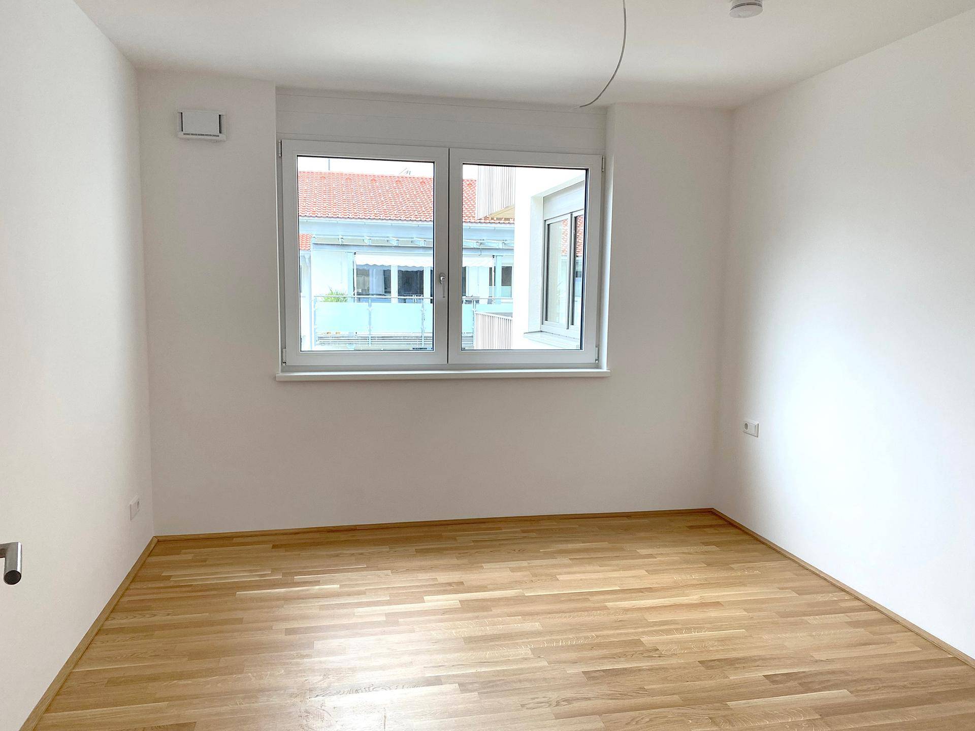 Helles Schlafzimmer mit Eichenparkett und Fenster, ausgestattet mit Außenrollläden für Privatsphäre.