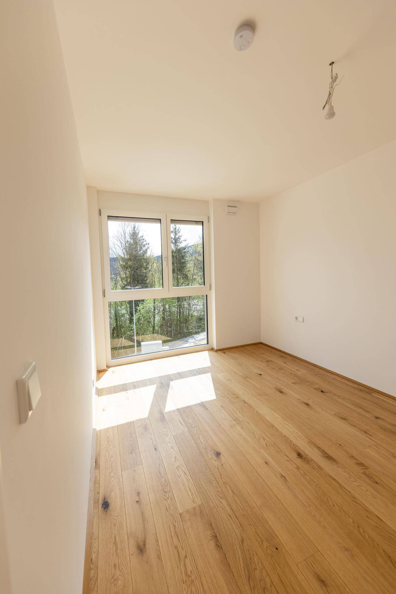 Heller Raum mit Holzboden und Fenster, durch das viel Sonnenlicht einfällt.